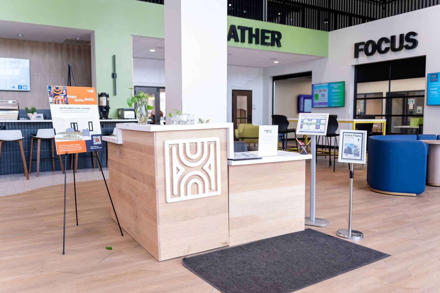 Modern office reception desk with light wood finish, featuring GATHER and FOCUS branded meeting rooms in bright lobby.