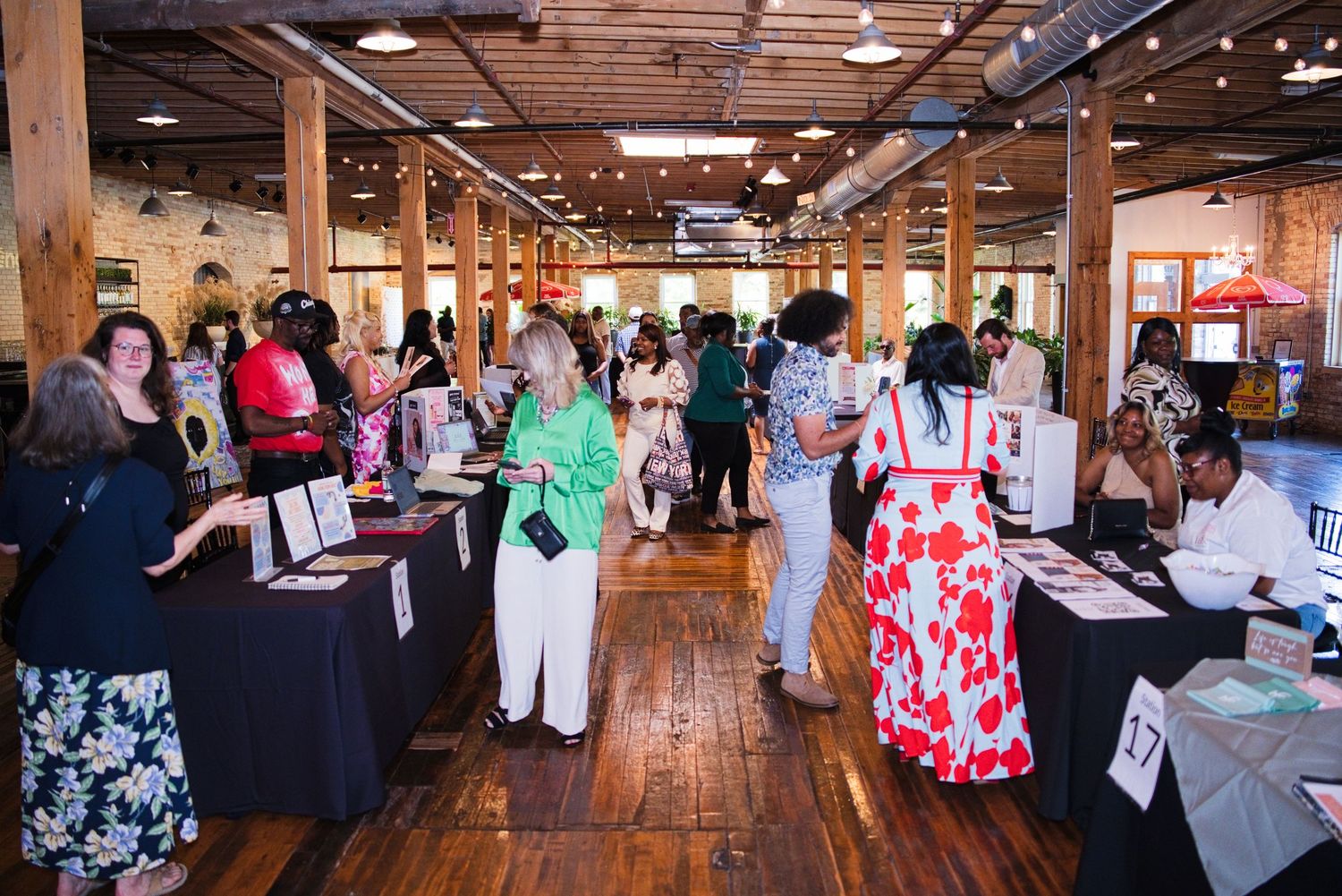 Guests browse vendor tables at a women's networking event inside a rustic wooden venue.