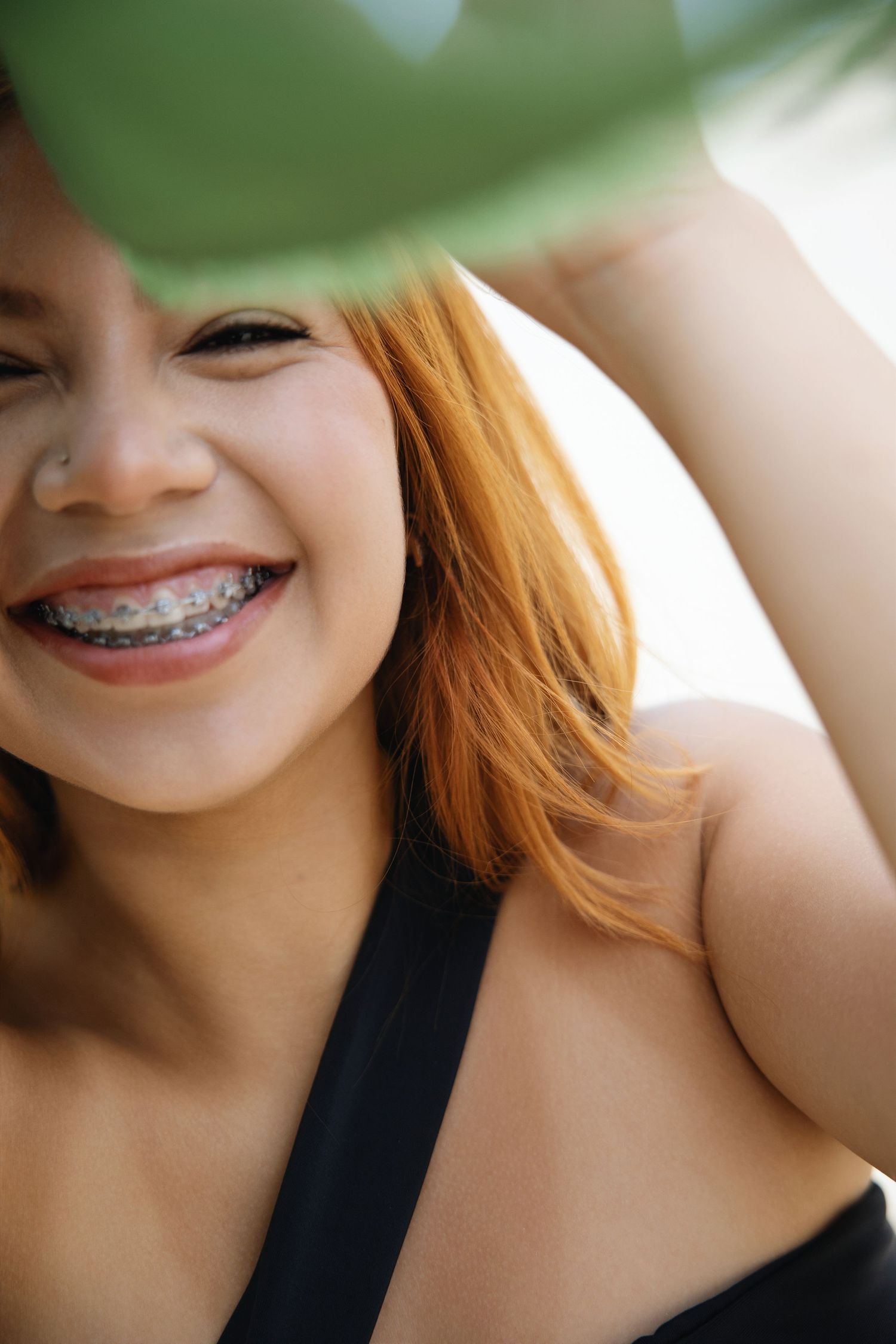 Close up portrait showing bright smile with braces against natural green background.