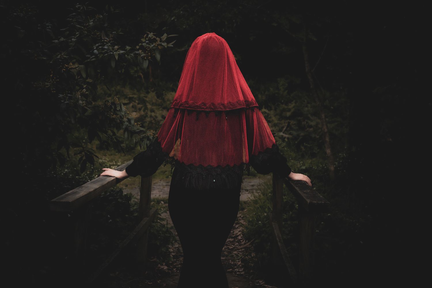 A person in a red cape stands mysteriously in a dark forest setting creating an eerie atmosphere.