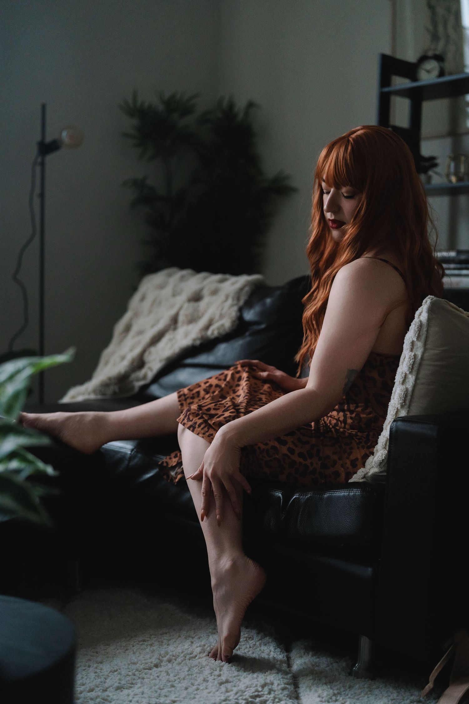 Person lounging on dark couch wearing animal print dress in dimly lit room.