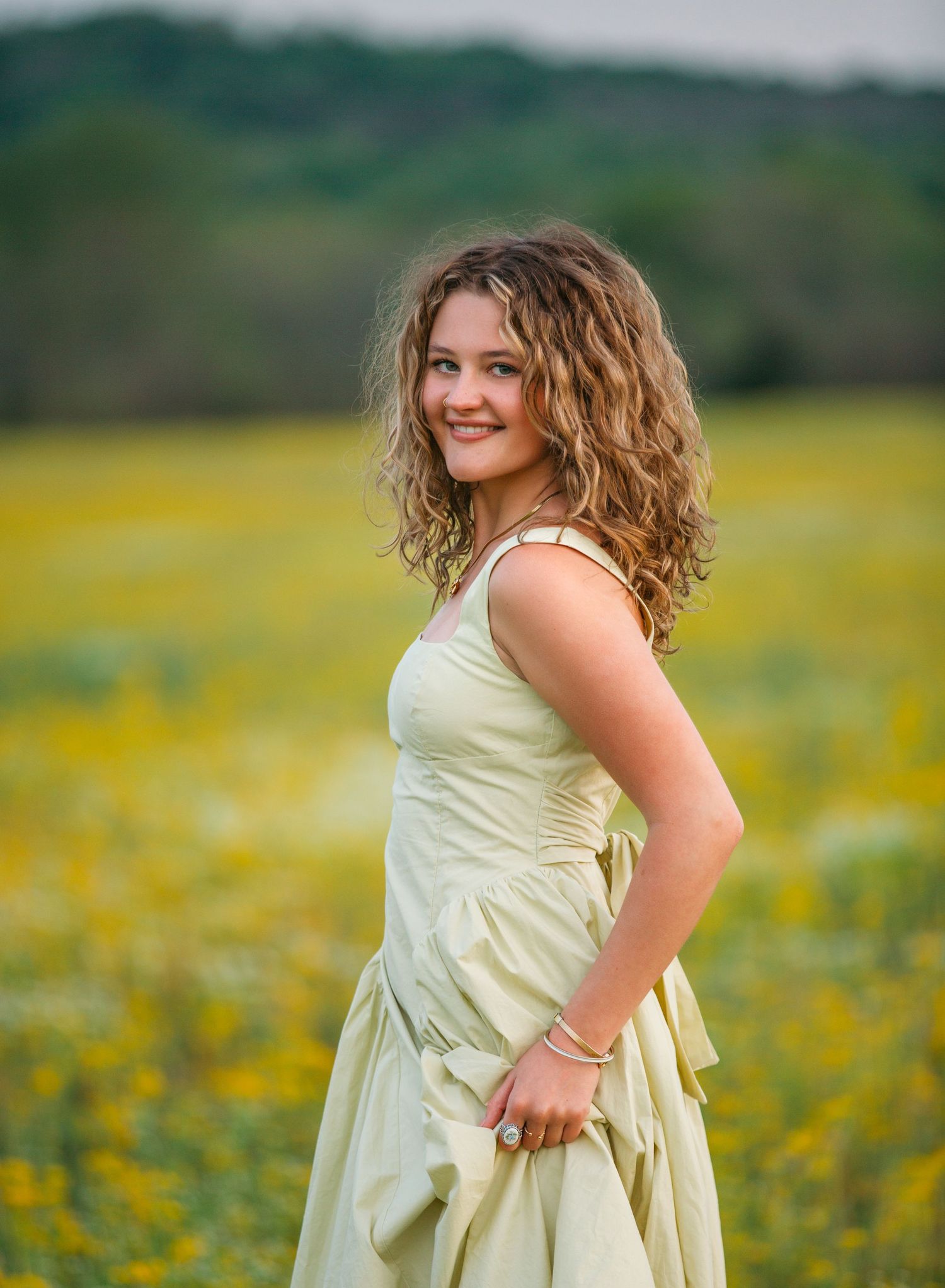 Person in a light yellow sundress poses in a field of blooming yellow wildflowers on a spring afternoon.