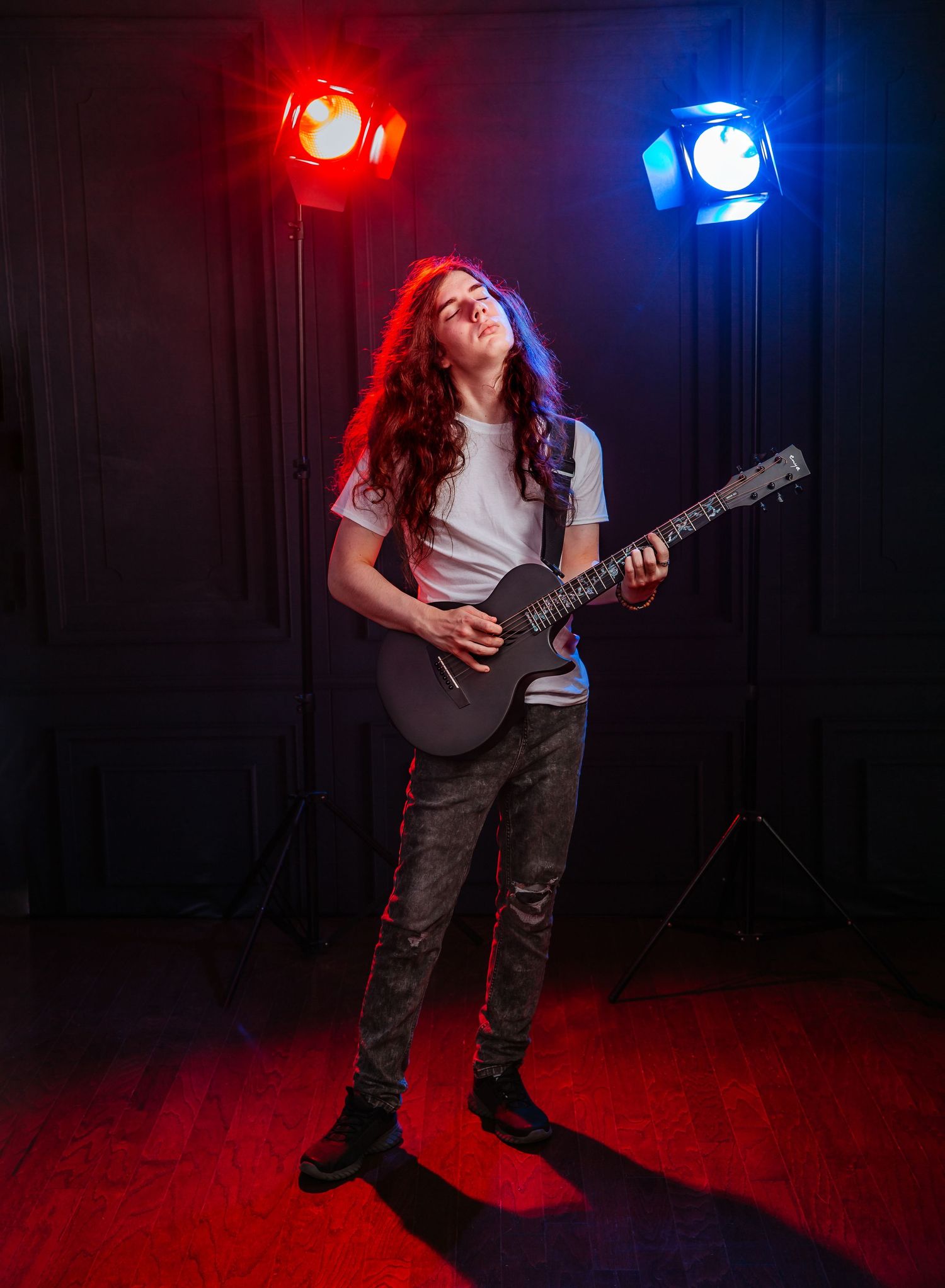 Musician playing electric guitar under dramatic red and blue stage lighting.