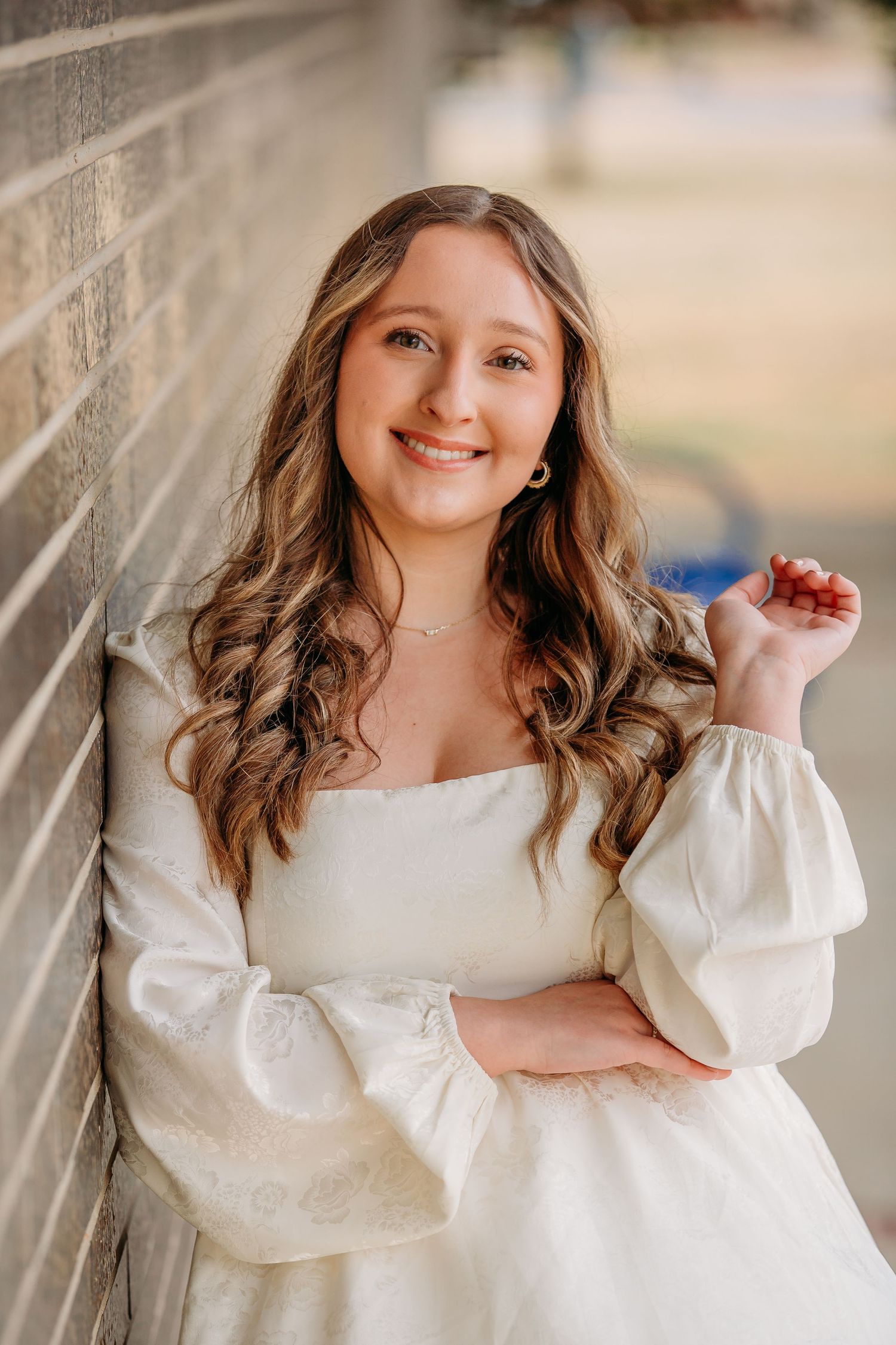 A person in a white dress with puff sleeves poses against a brick wall with natural curly hair.