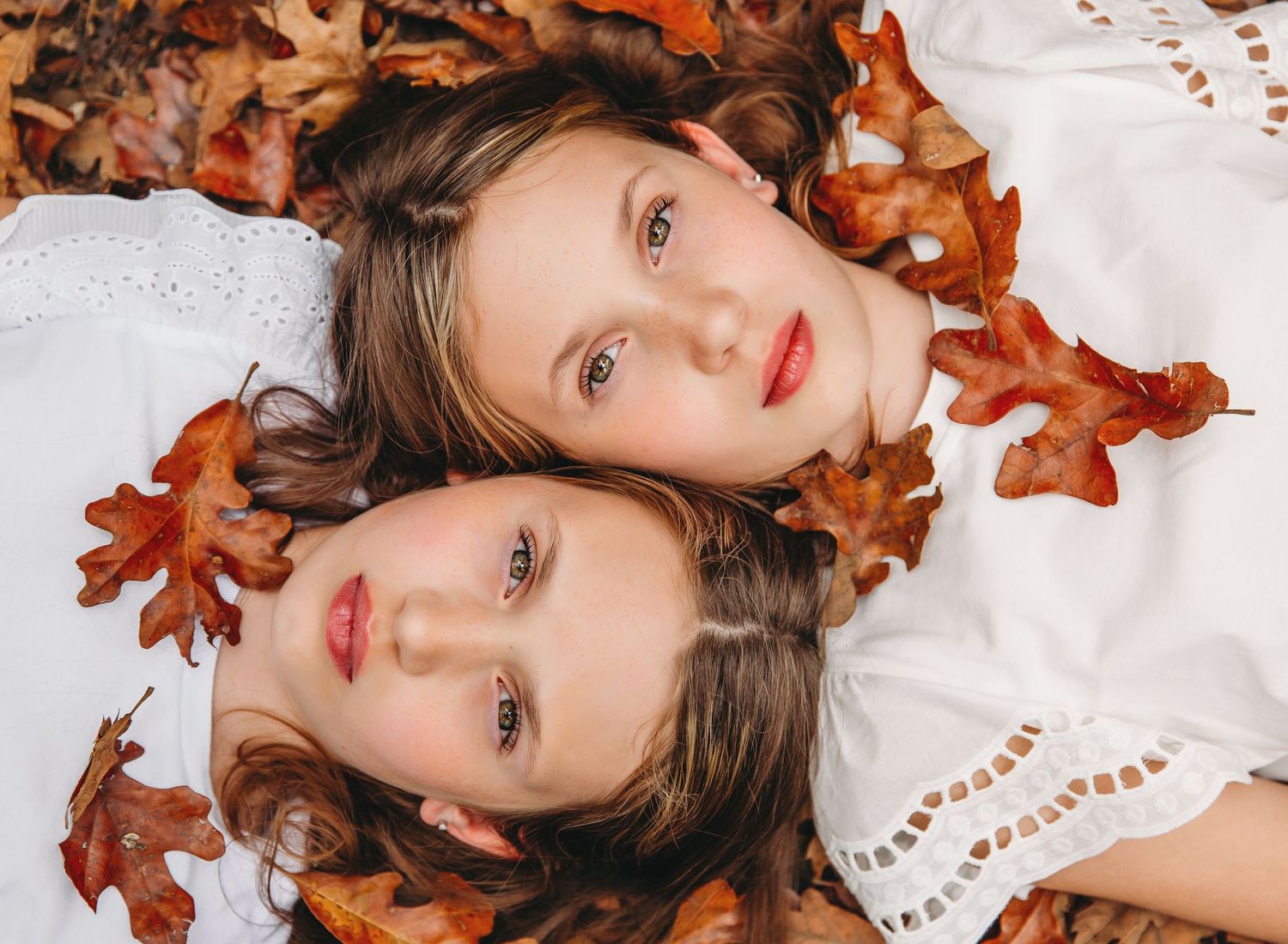 Two people lie among fall leaves wearing white clothing in an artistic portrait.
