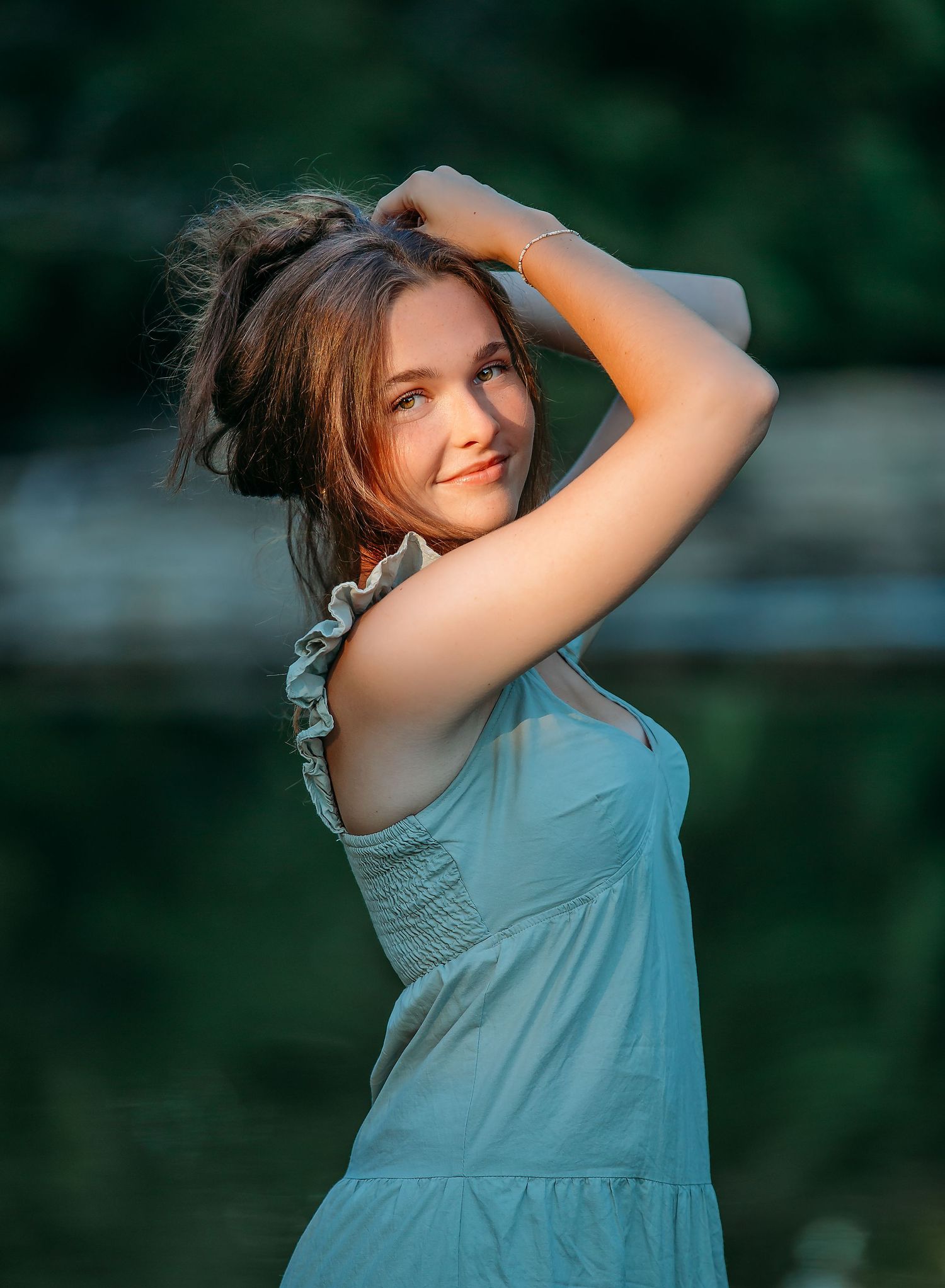 A person wearing a blue summer dress poses playfully against a blurred natural backdrop.