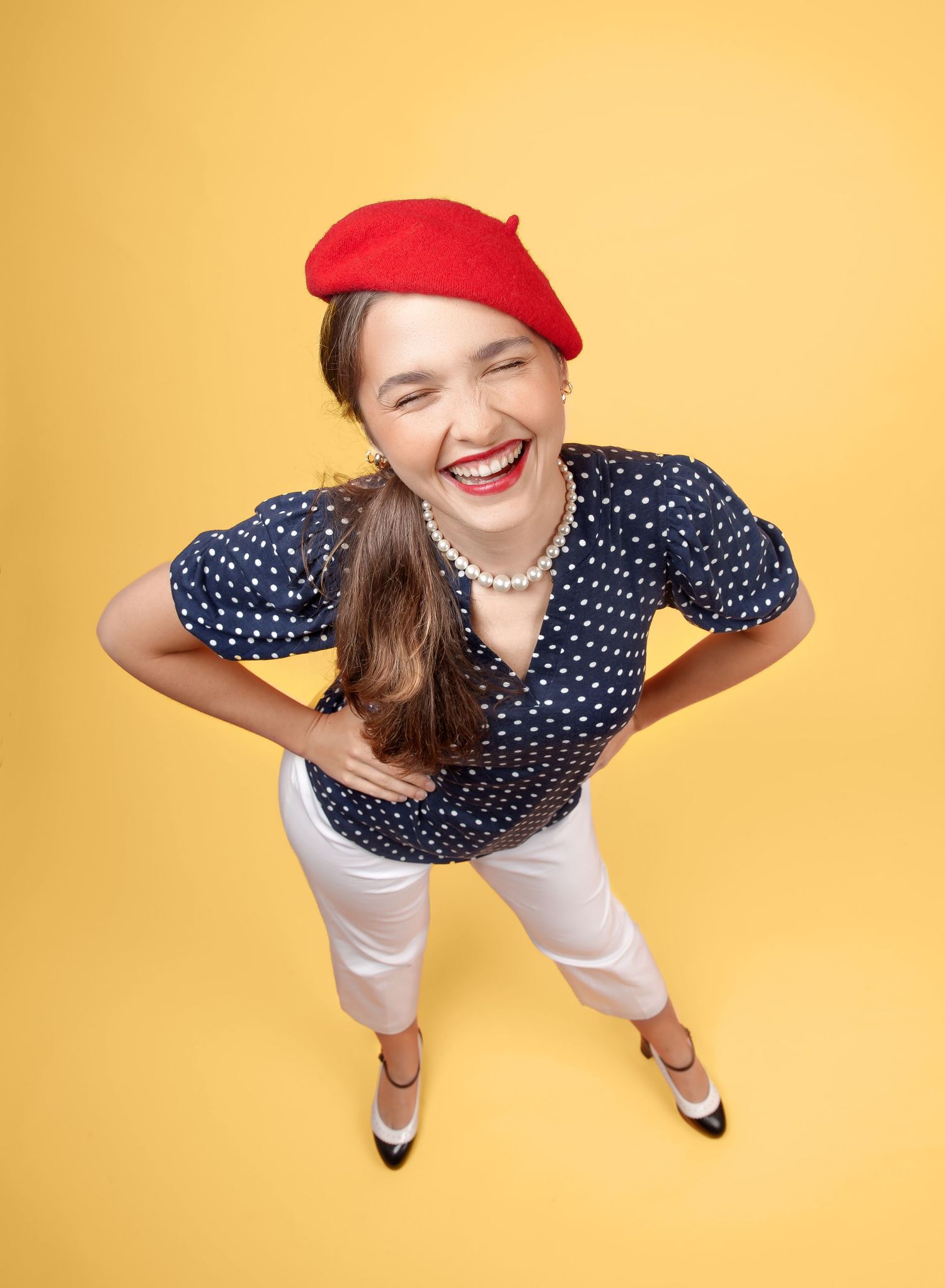 Person wearing polka dot shirt and red cap stands against yellow backdrop in playful overhead poses.