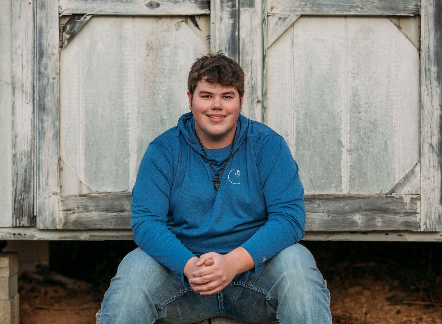 Person in blue hoodie sits on rustic wooden bench against weathered white wall.