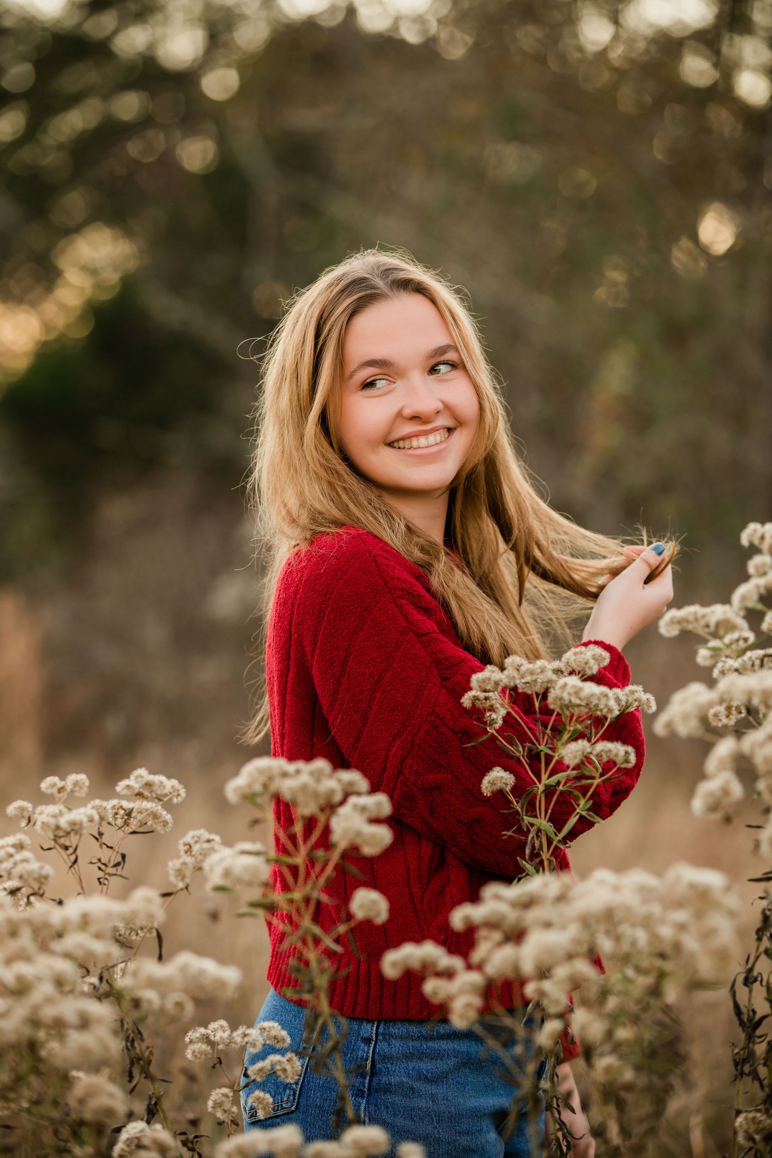Autumn portrait in red sweater among wild dried flowers at golden hour.
