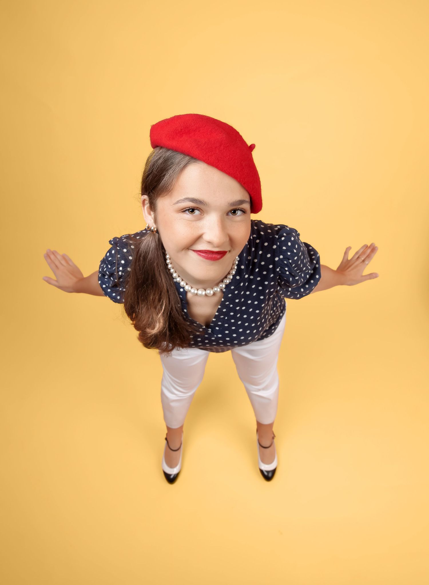 Person in red beret and polka dot top poses playfully from above against yellow backdrop.