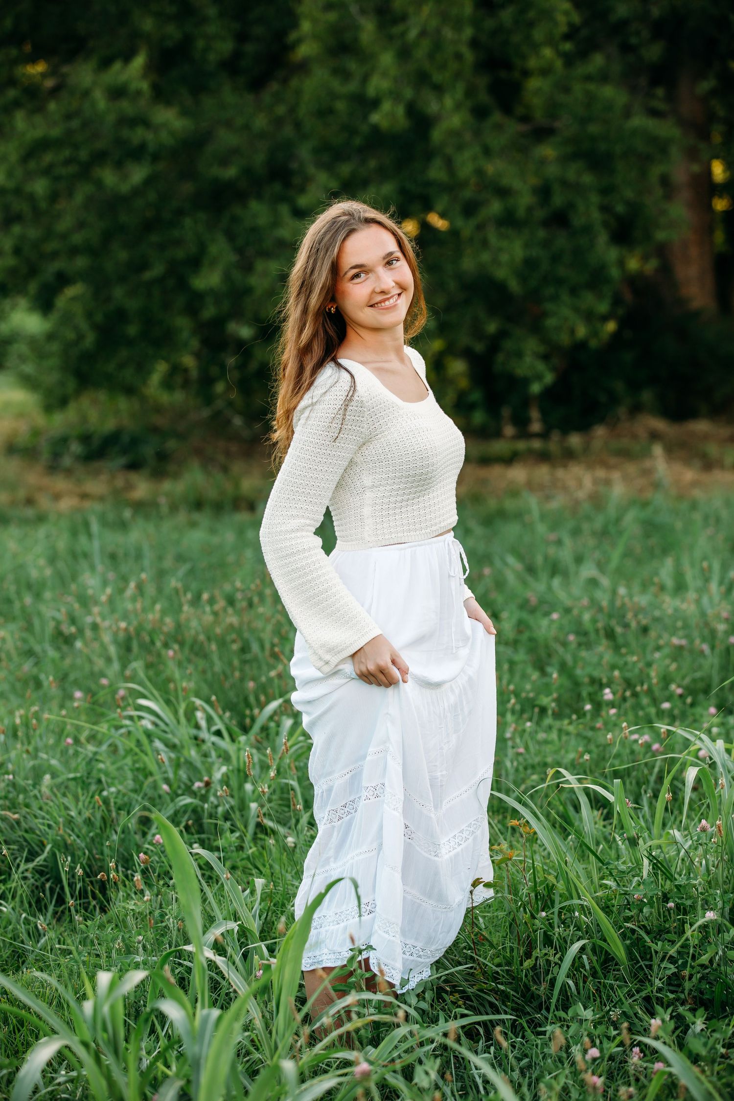 A person in a flowing white dress twirls playfully in a lush green meadow on a sunny summer day.