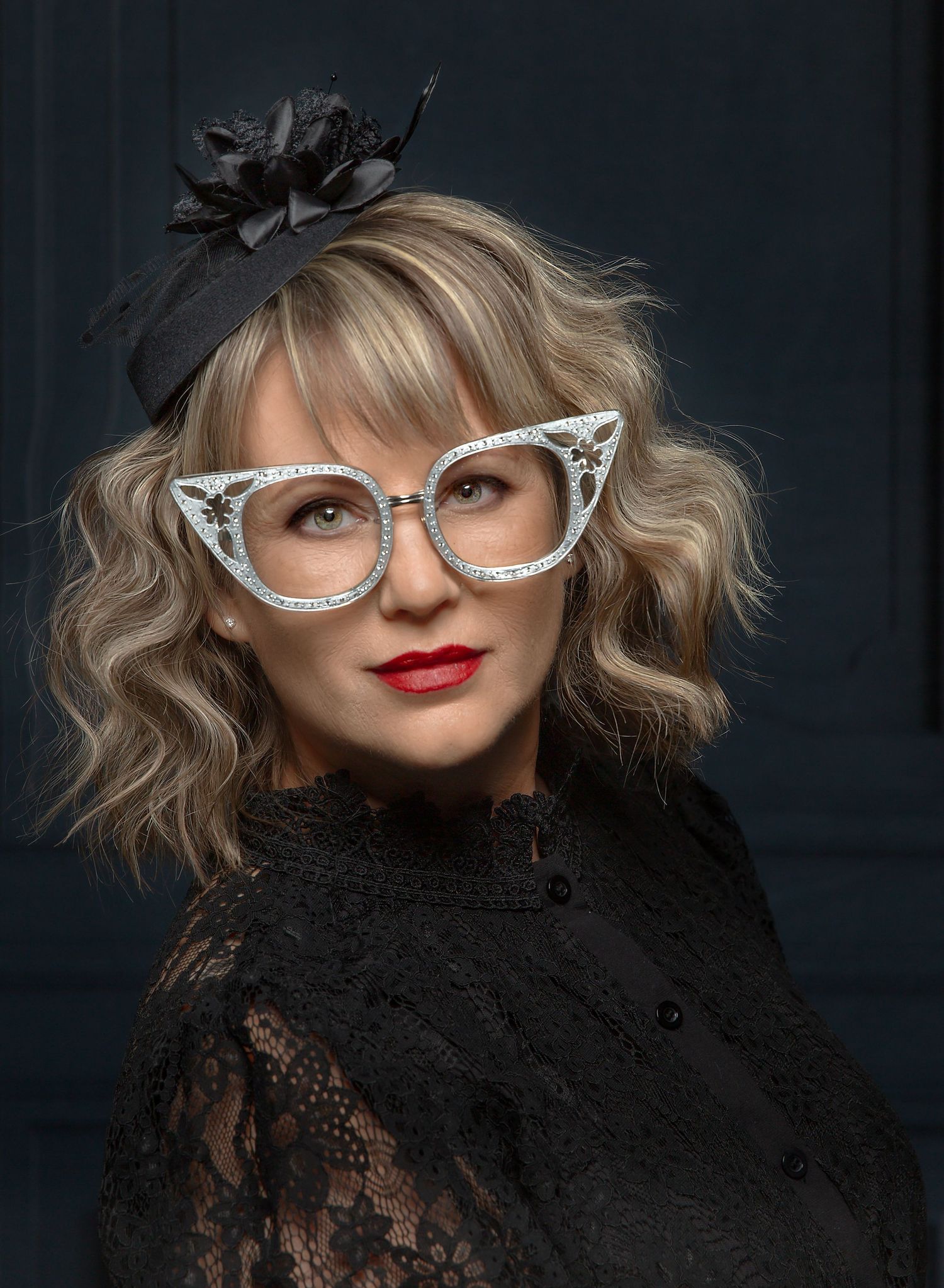A glamorous vintage-inspired portrait featuring cat-eye glasses and black lace against a dark backdrop.