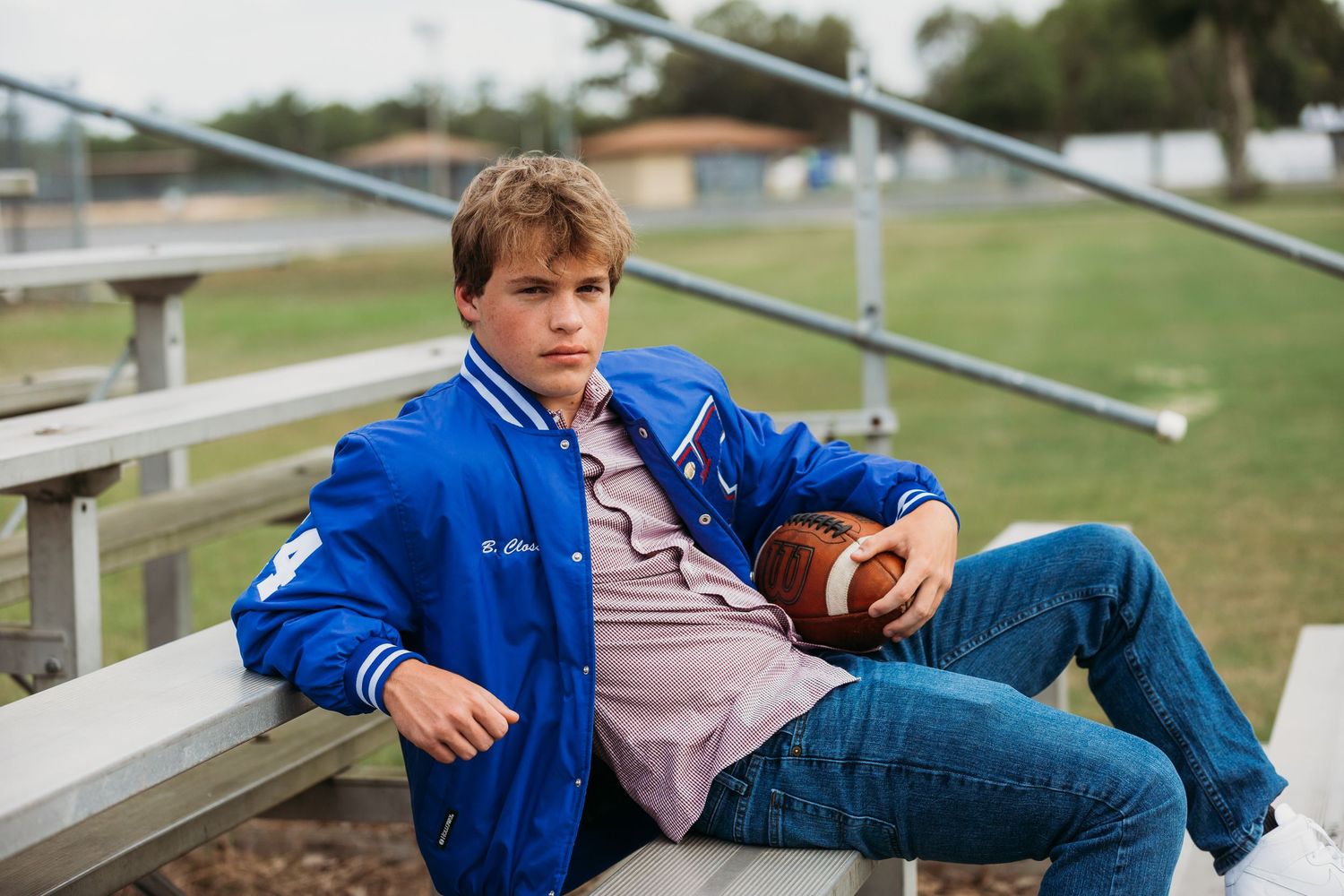 Athletic portrait on bleachers with varsity jacket and football.