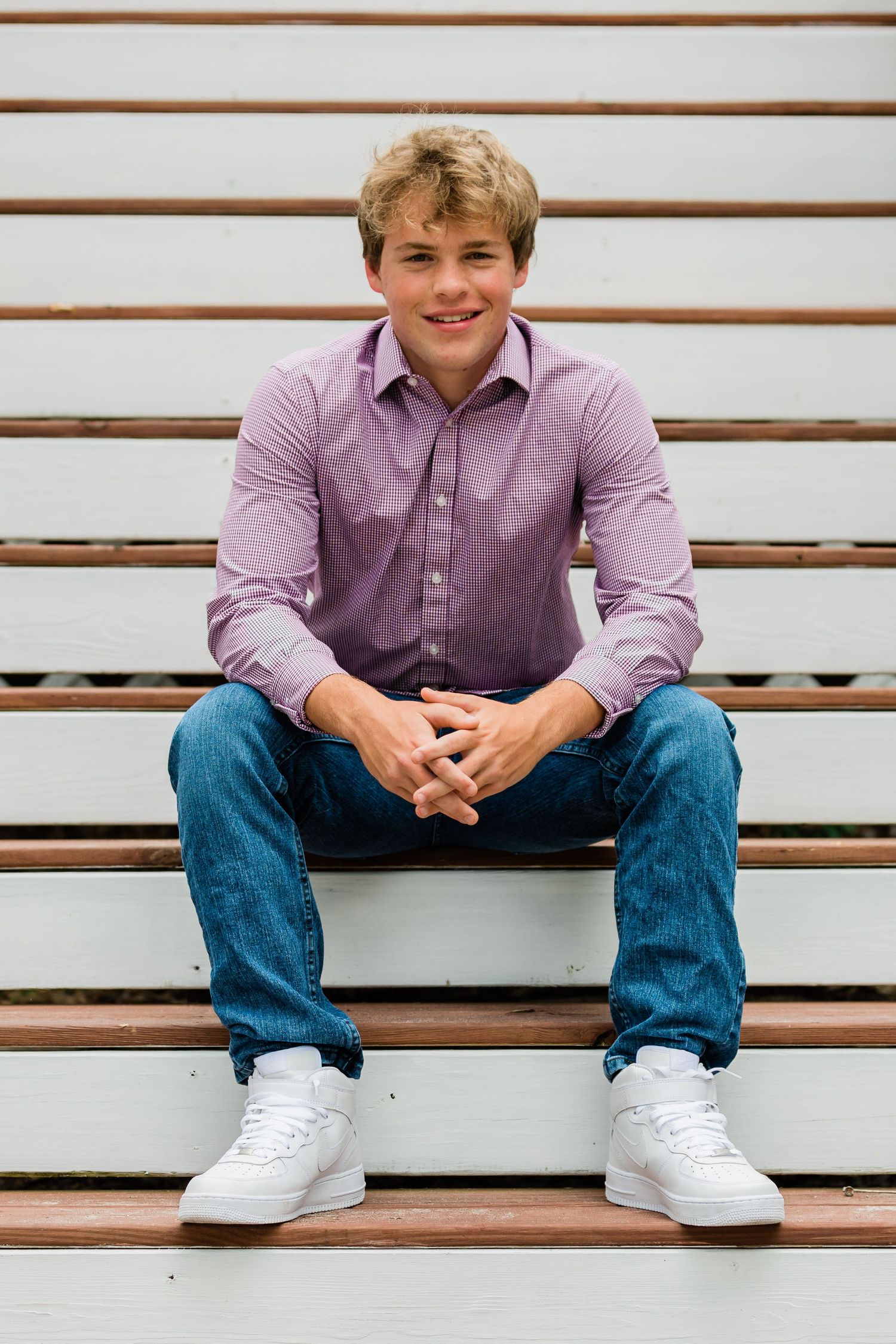 Casual portrait on wooden bleachers wearing purple button-down shirt and jeans.