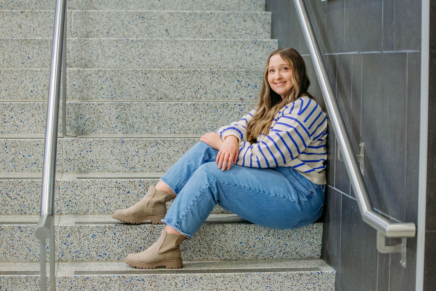 Someone in blue jeans and brown boots lies casually on concrete steps outside a building.