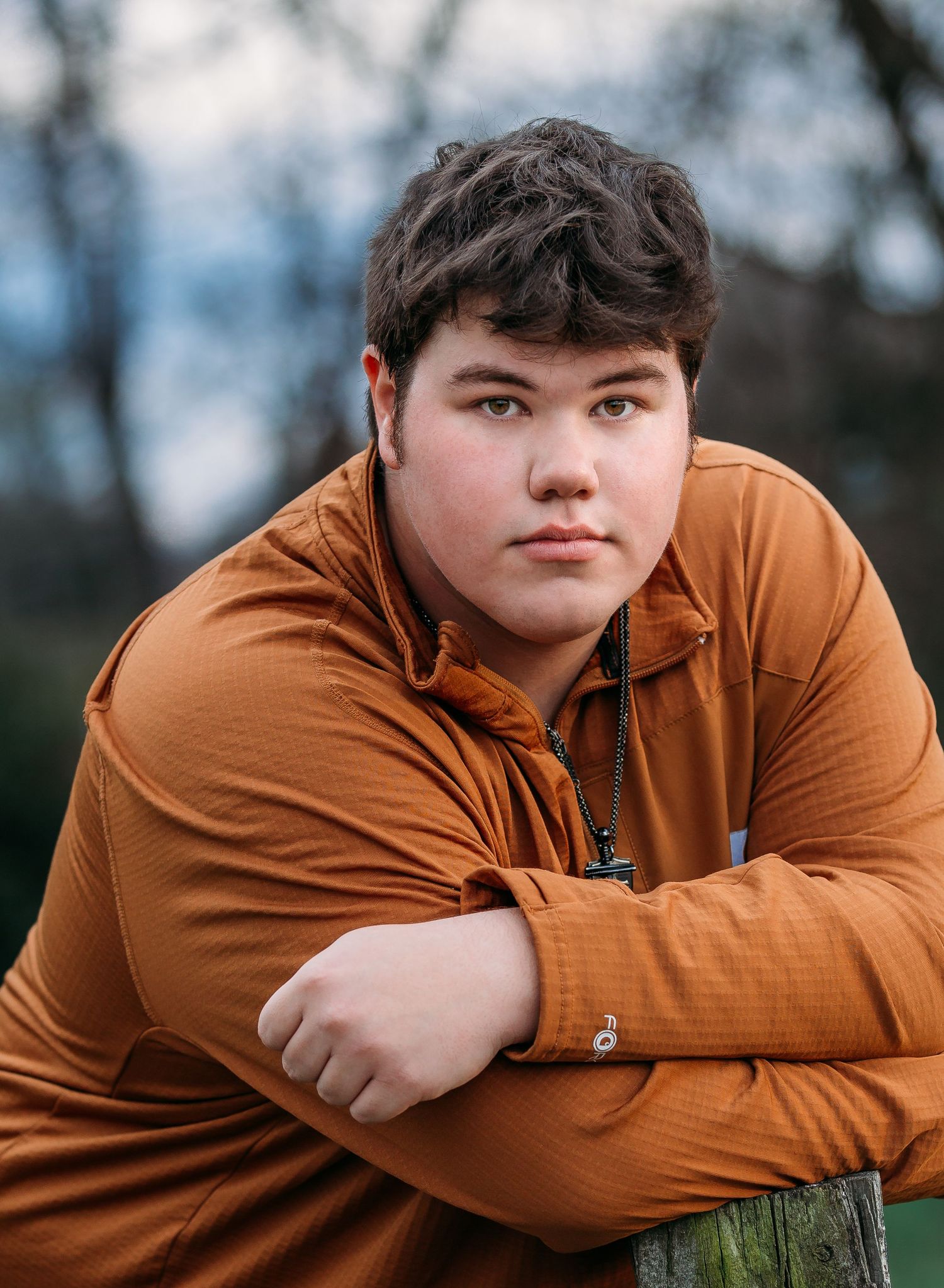 Young person in burnt orange hoodie poses outdoors in a series of artistic portrait shots against blurred natural background.