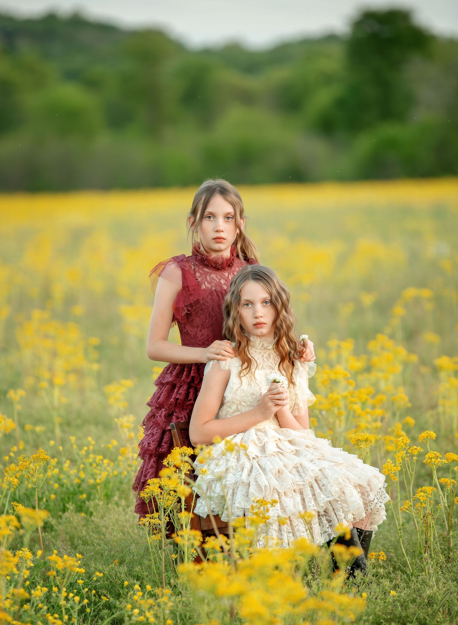Two figures pose elegantly in a field of blooming yellow wildflowers at sunset.