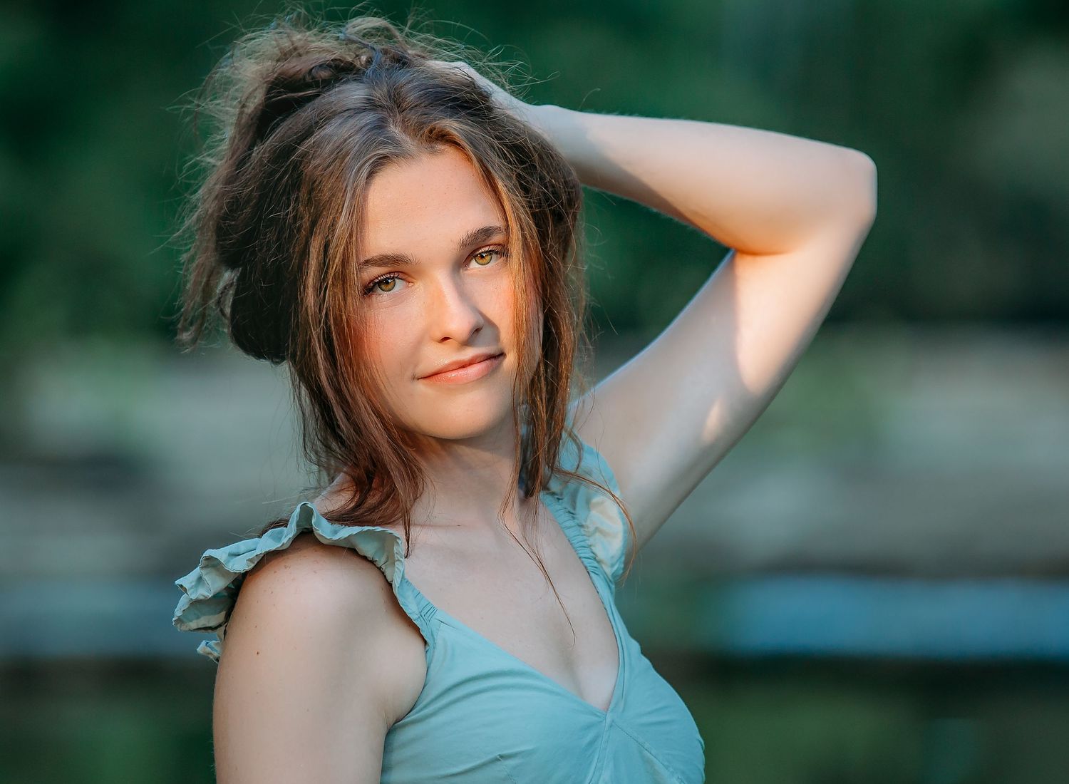 A soft portrait in natural light shows someone with windswept hair wearing a turquoise top against a blurred outdoor background.