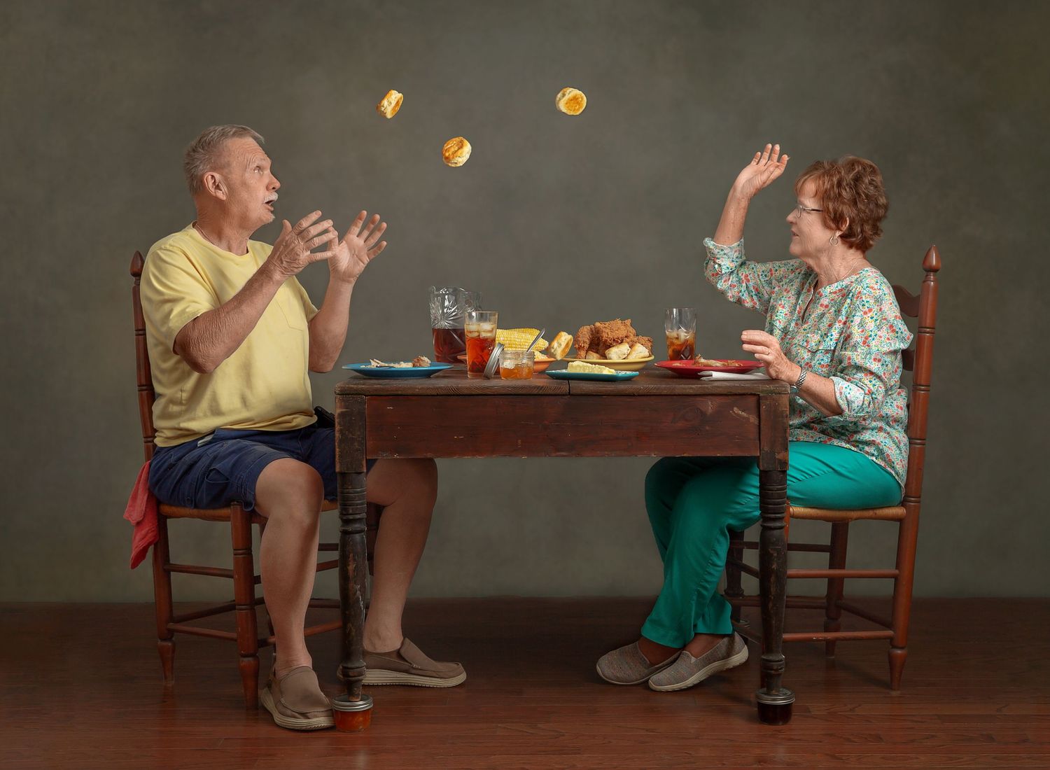 Two people seated at a table throwing biscuits during a playful dining scene.