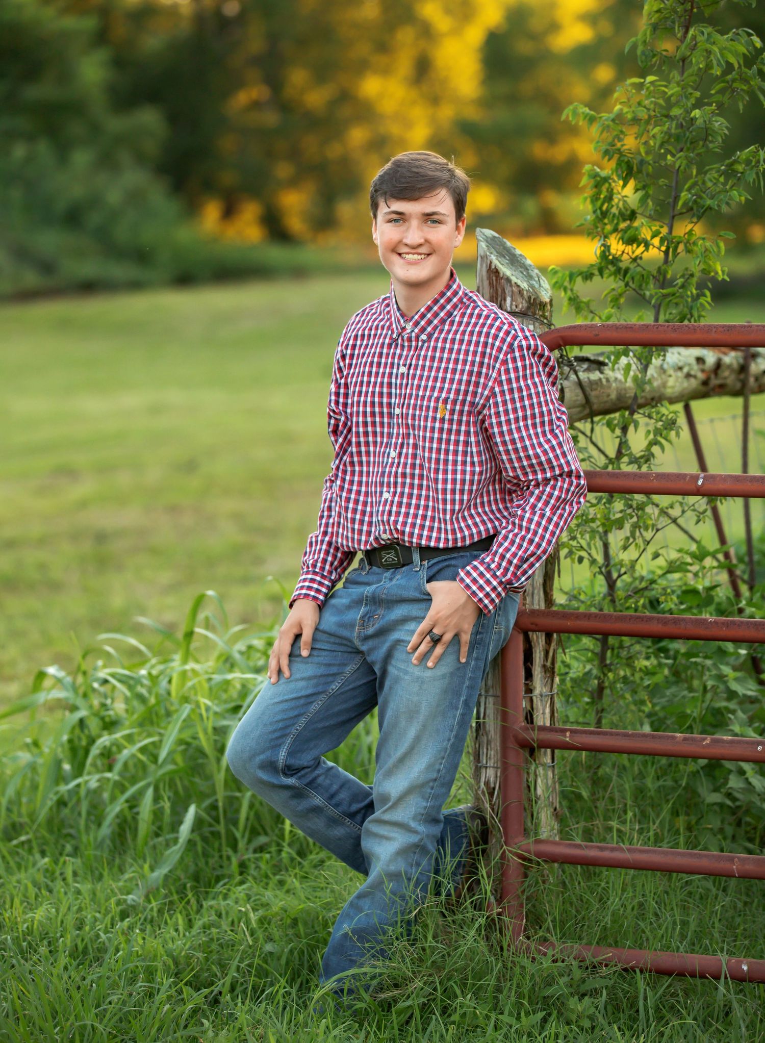 Country style portrait in red checkered shirt leaning against rustic fence with autumn colors.