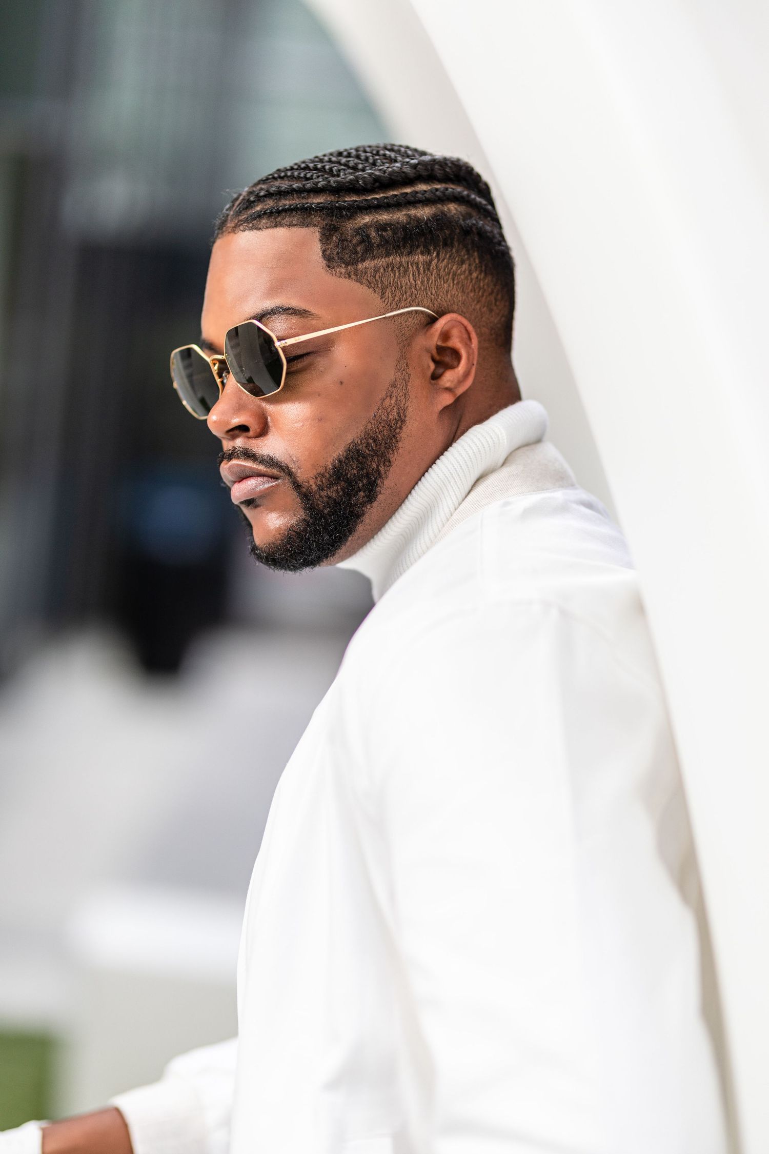 Fashion portrait in white attire and sunglasses with modern architecture backdrop.