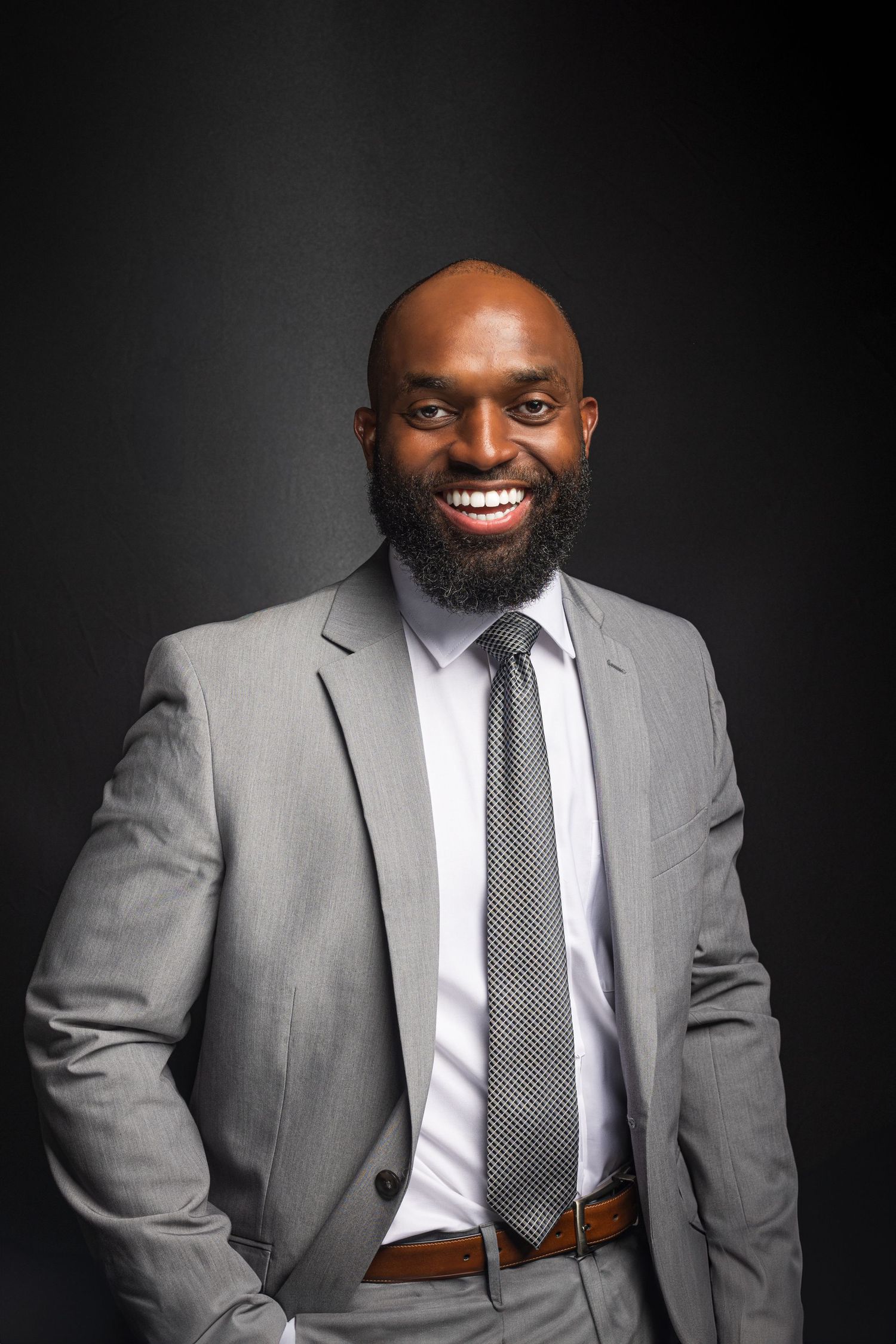 Professional headshots showing someone smiling in a grey suit and striped tie on black background.