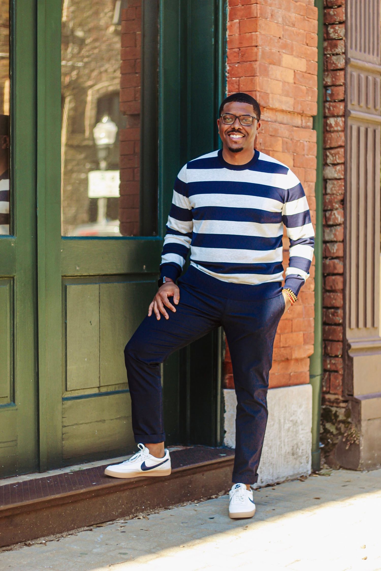 Casual fashion photos in navy and white striped shirt against brick storefront with green trim.