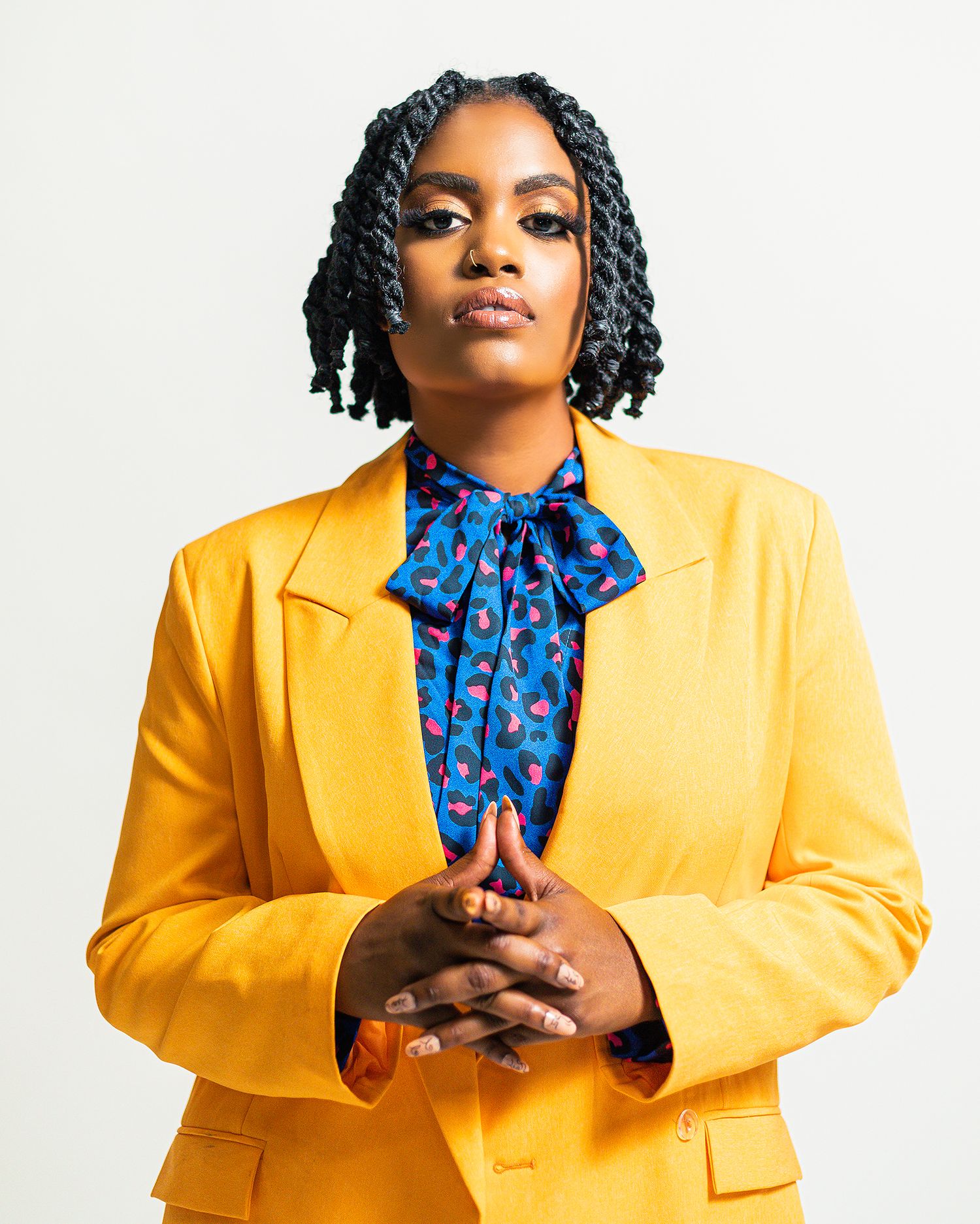 Studio fashion portrait in yellow blazer and blue patterned neck tie against white backdrop.
