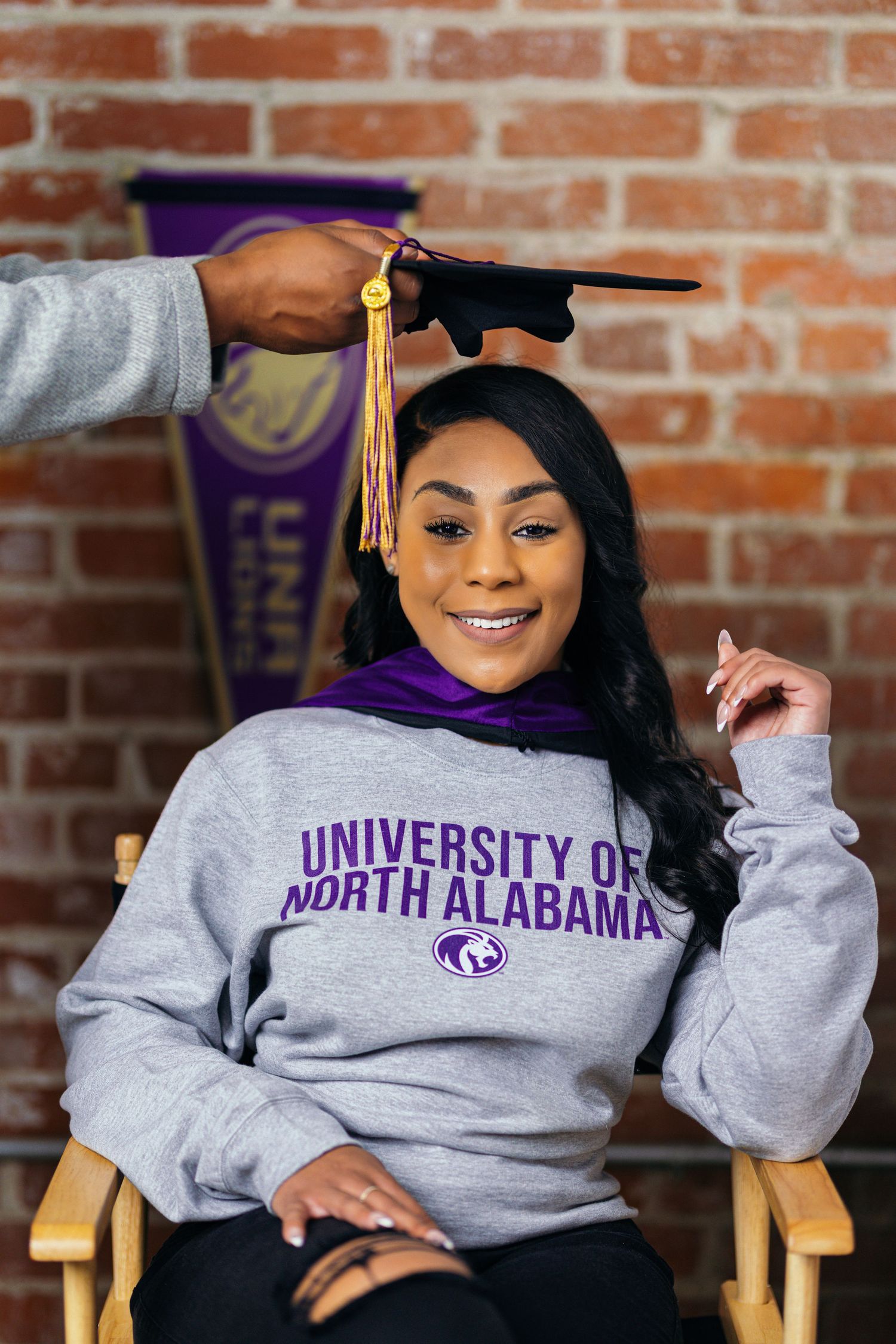 Graduate photos in University of North Alabama sweatshirt against brick wall background.