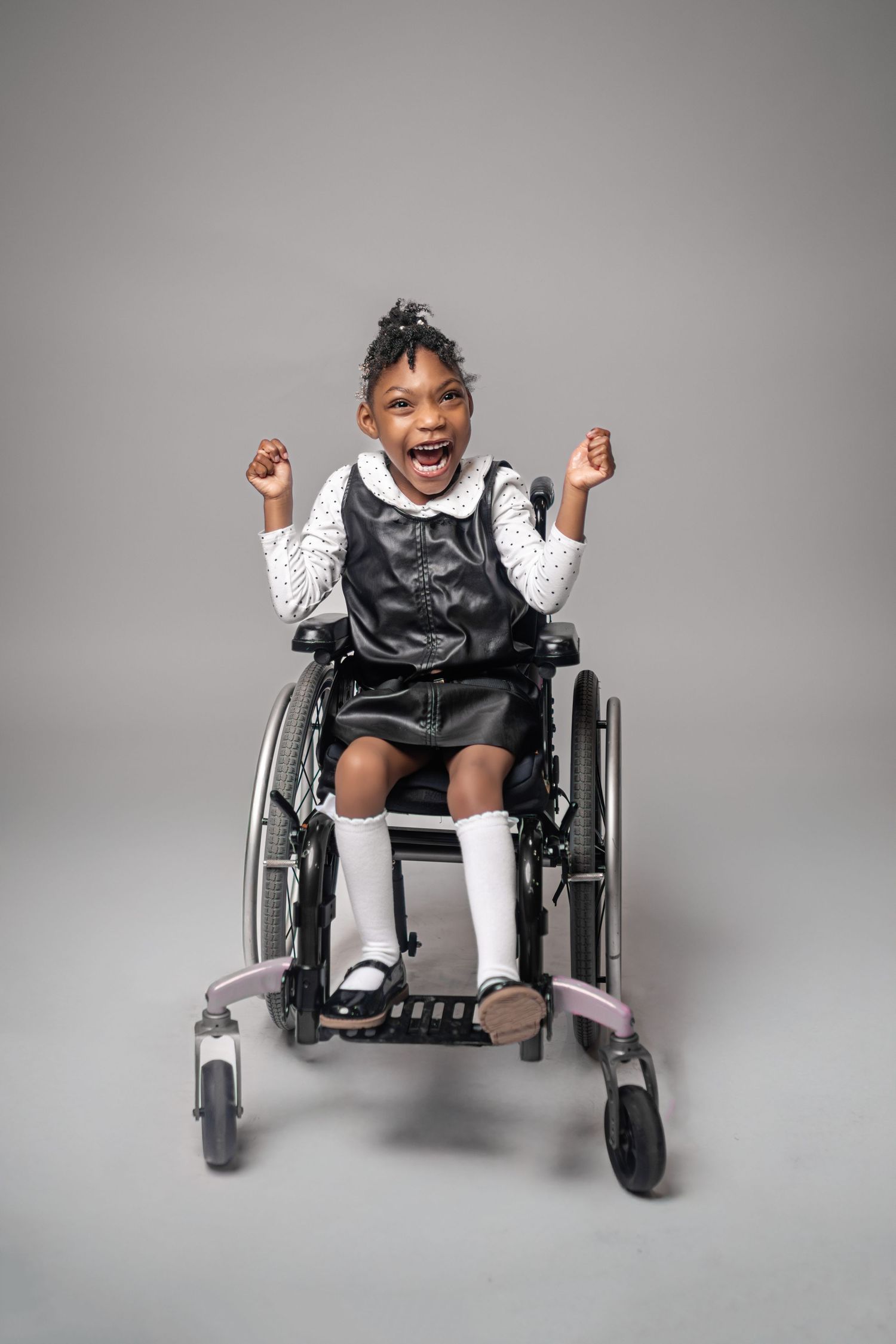 Happy child in wheelchair showing joyful expressions during studio photoshoot with gray background.