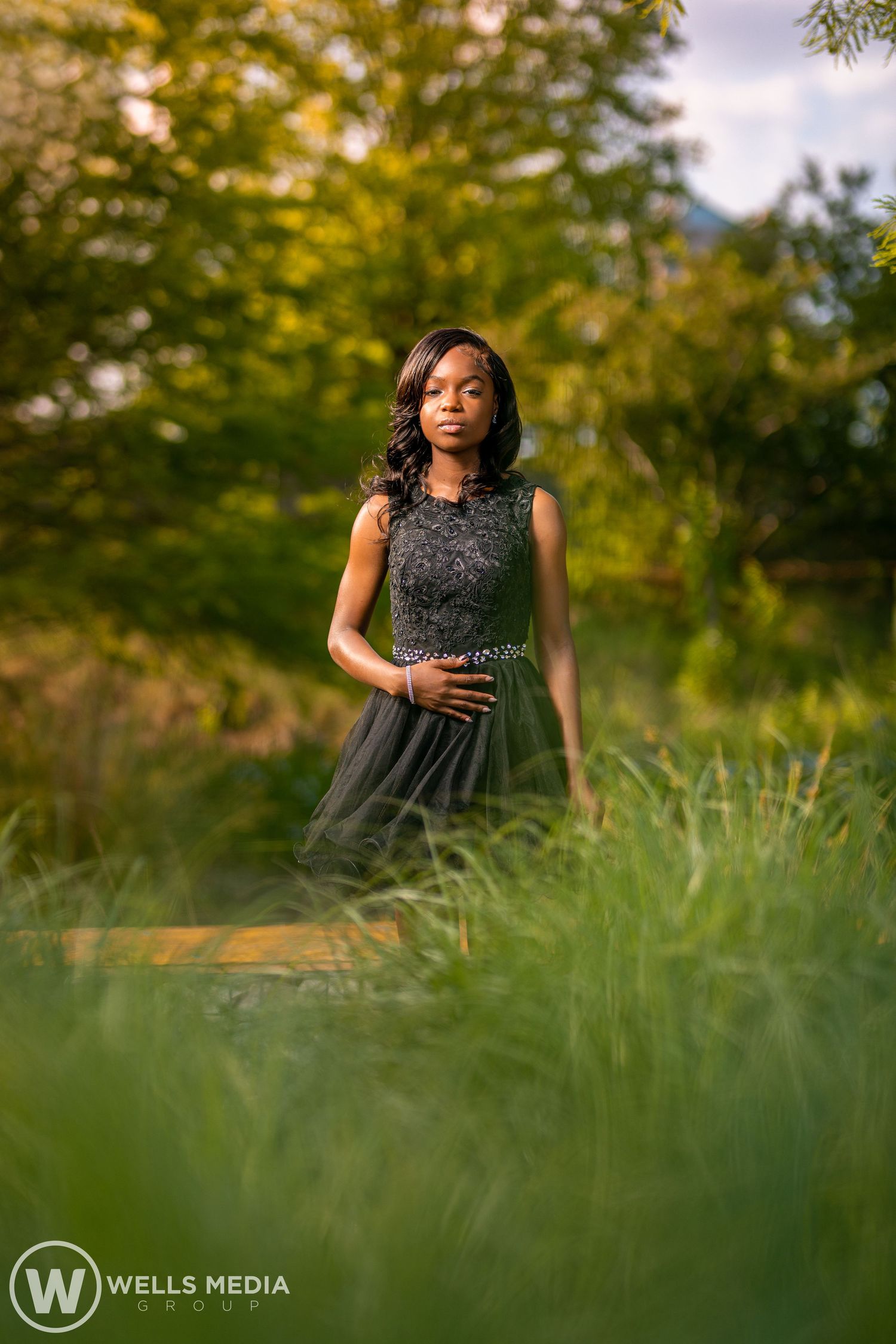 Portrait of someone in a dark dress amid tall grass and autumn foliage.