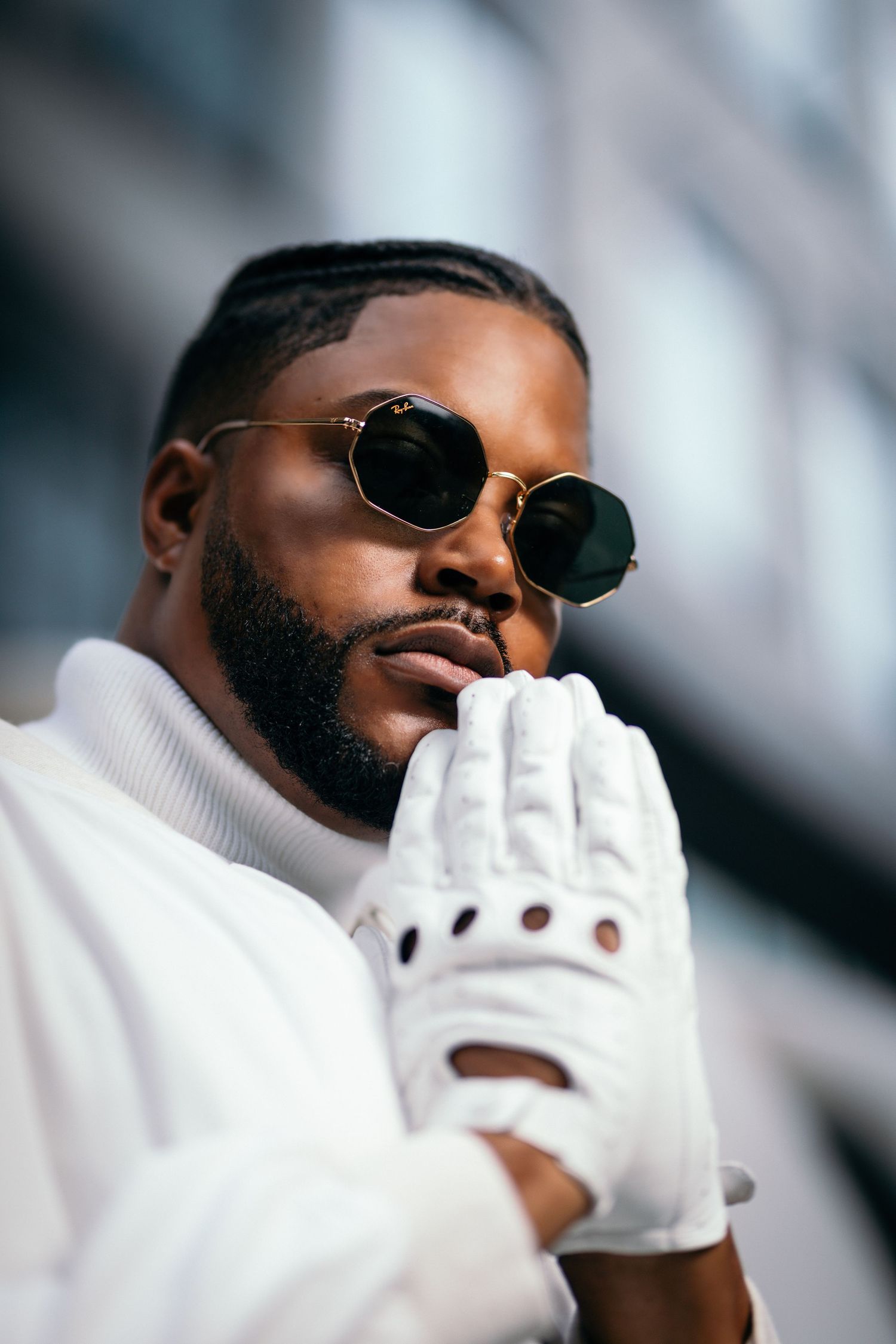Fashion portrait wearing white gloves and sunglasses against architectural backdrop.
