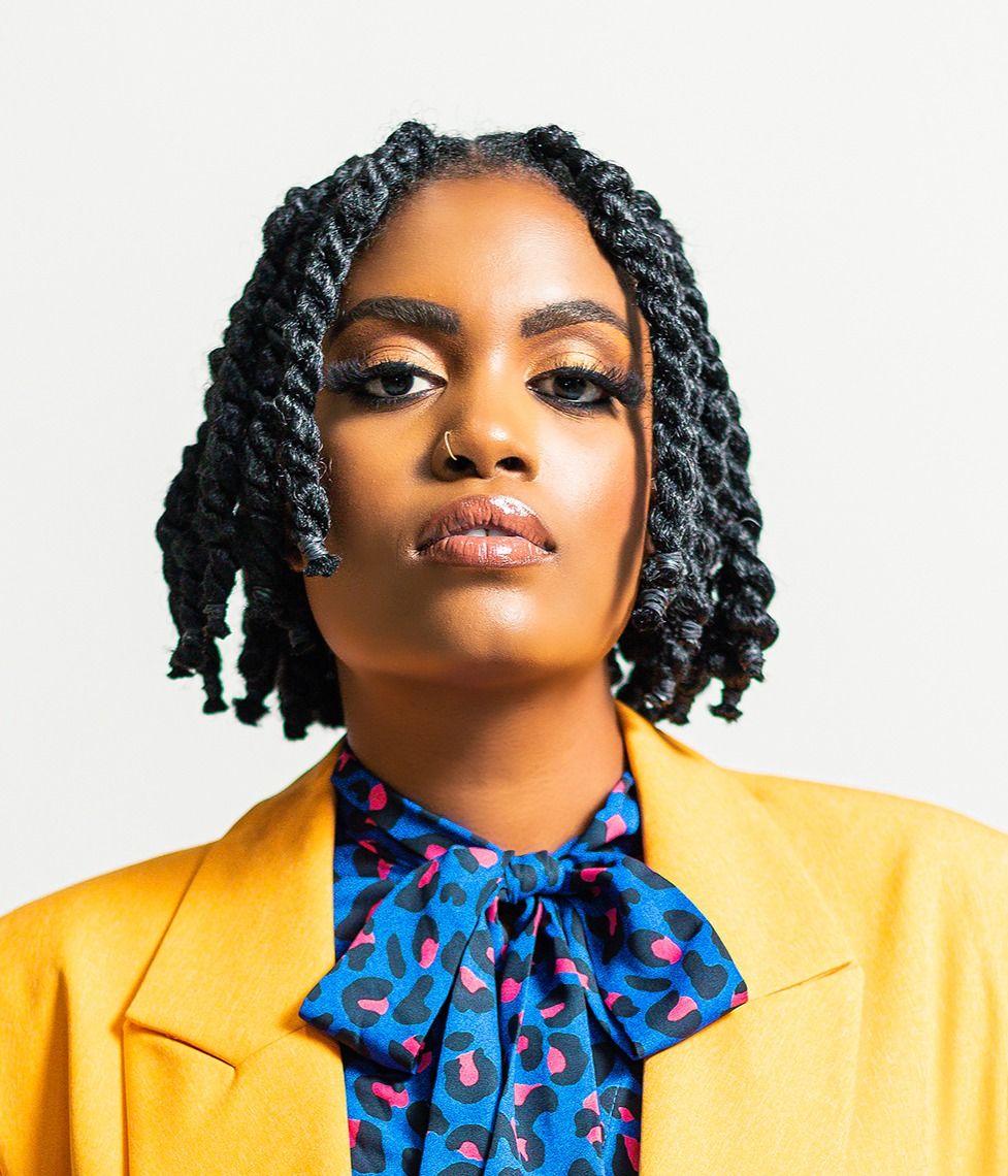 Professional studio portrait in bright yellow blazer and blue patterned tie against white background.