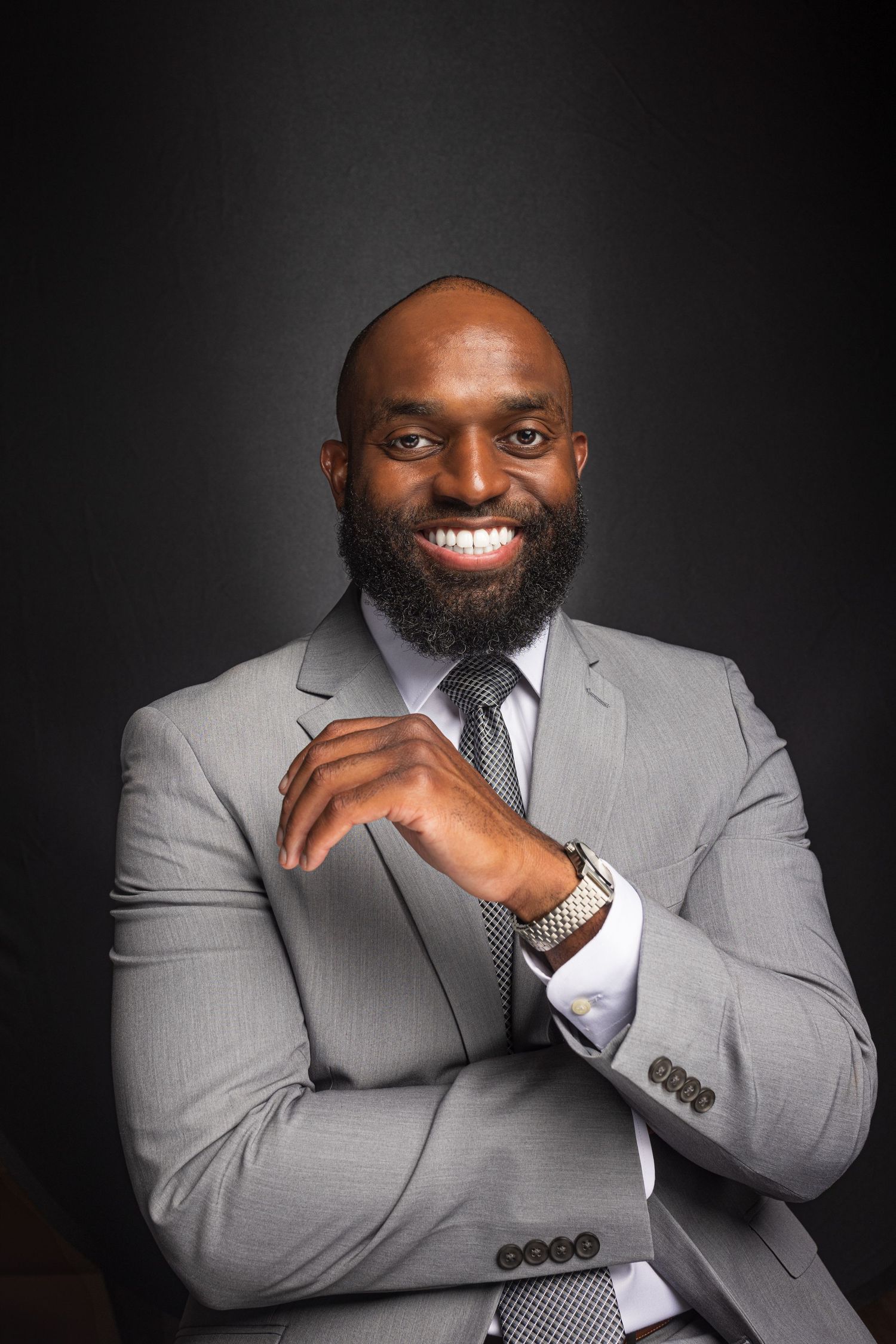 Professional studio portraits of someone in a light grey suit with a dark tie against a black background.