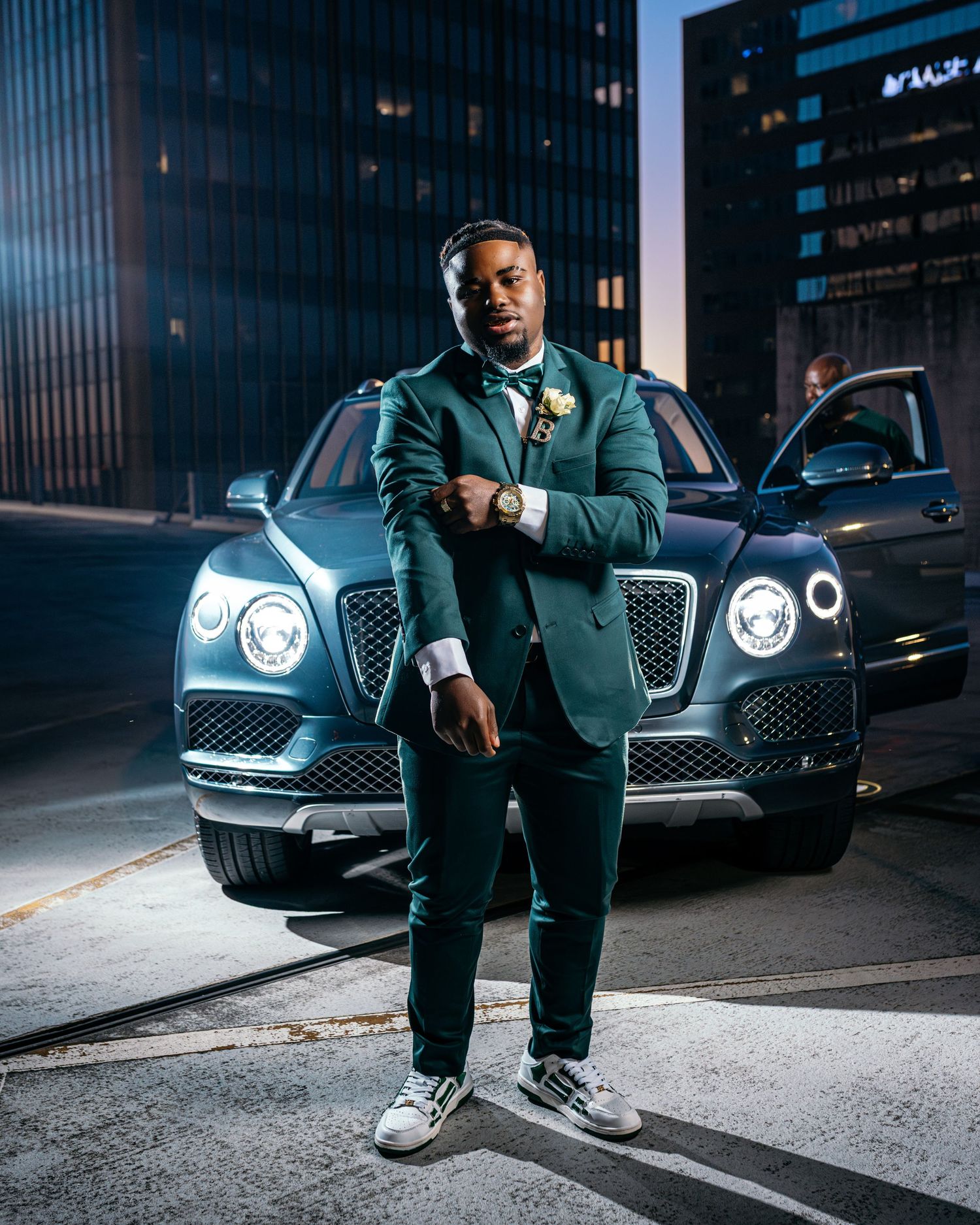 Low-angle shots of person in green suit with luxury cars and city buildings in background.