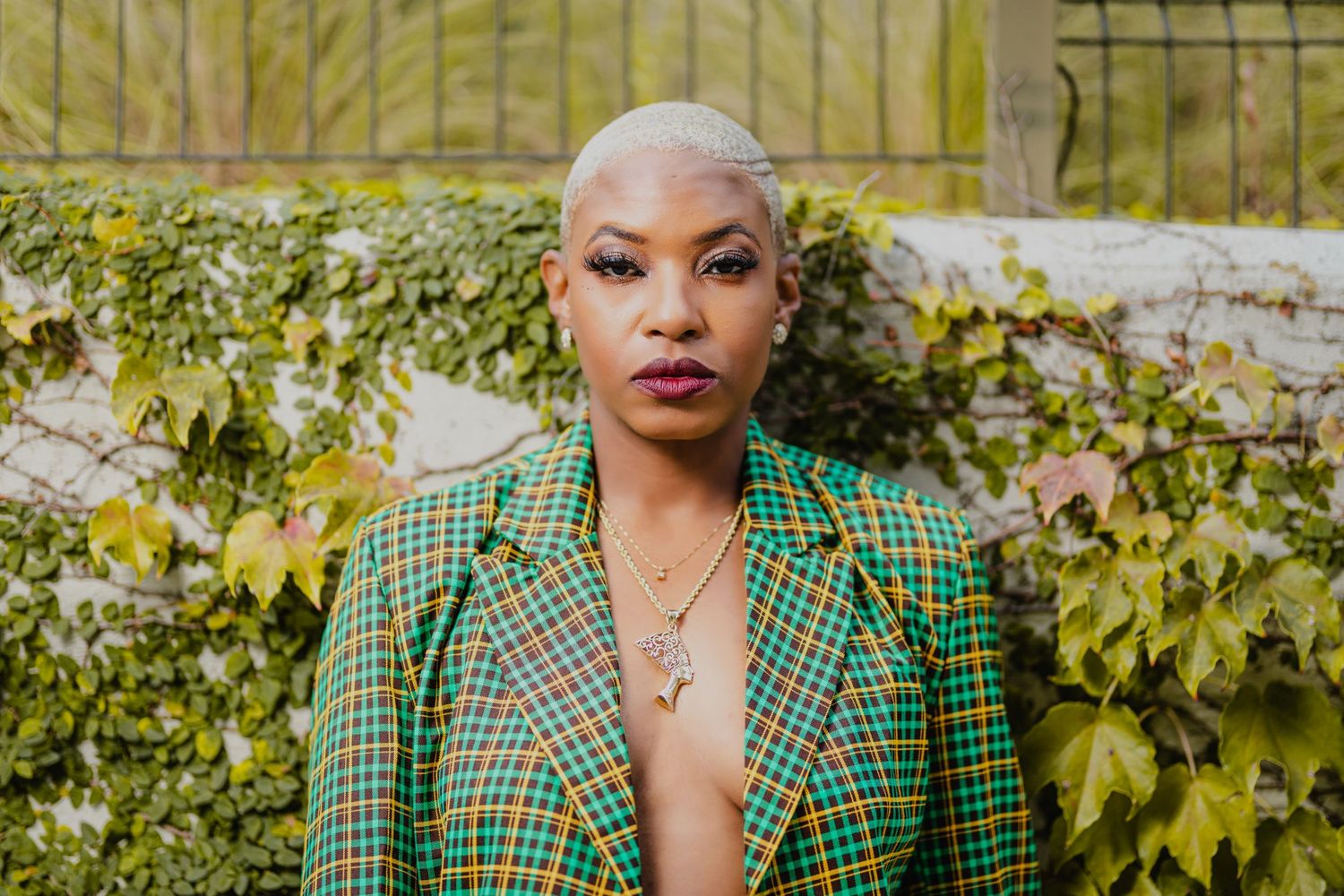 Professional outdoor portrait in green plaid blazer with natural foliage background.