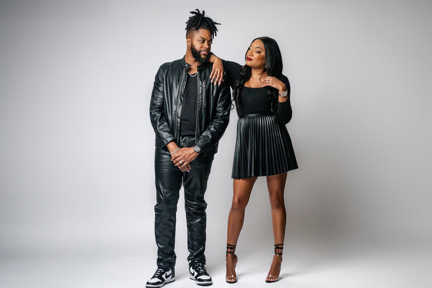 Couple in matching black outfits posing together for studio portraits.