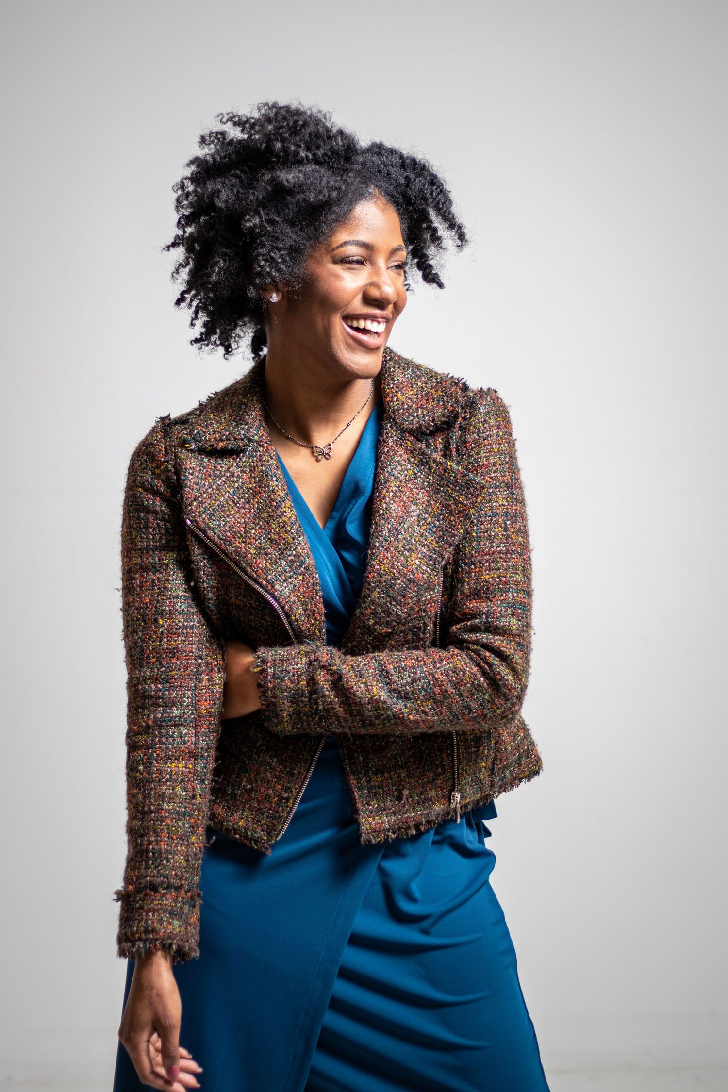 Happy woman in tweed jacket and blue dress laughing against neutral background.