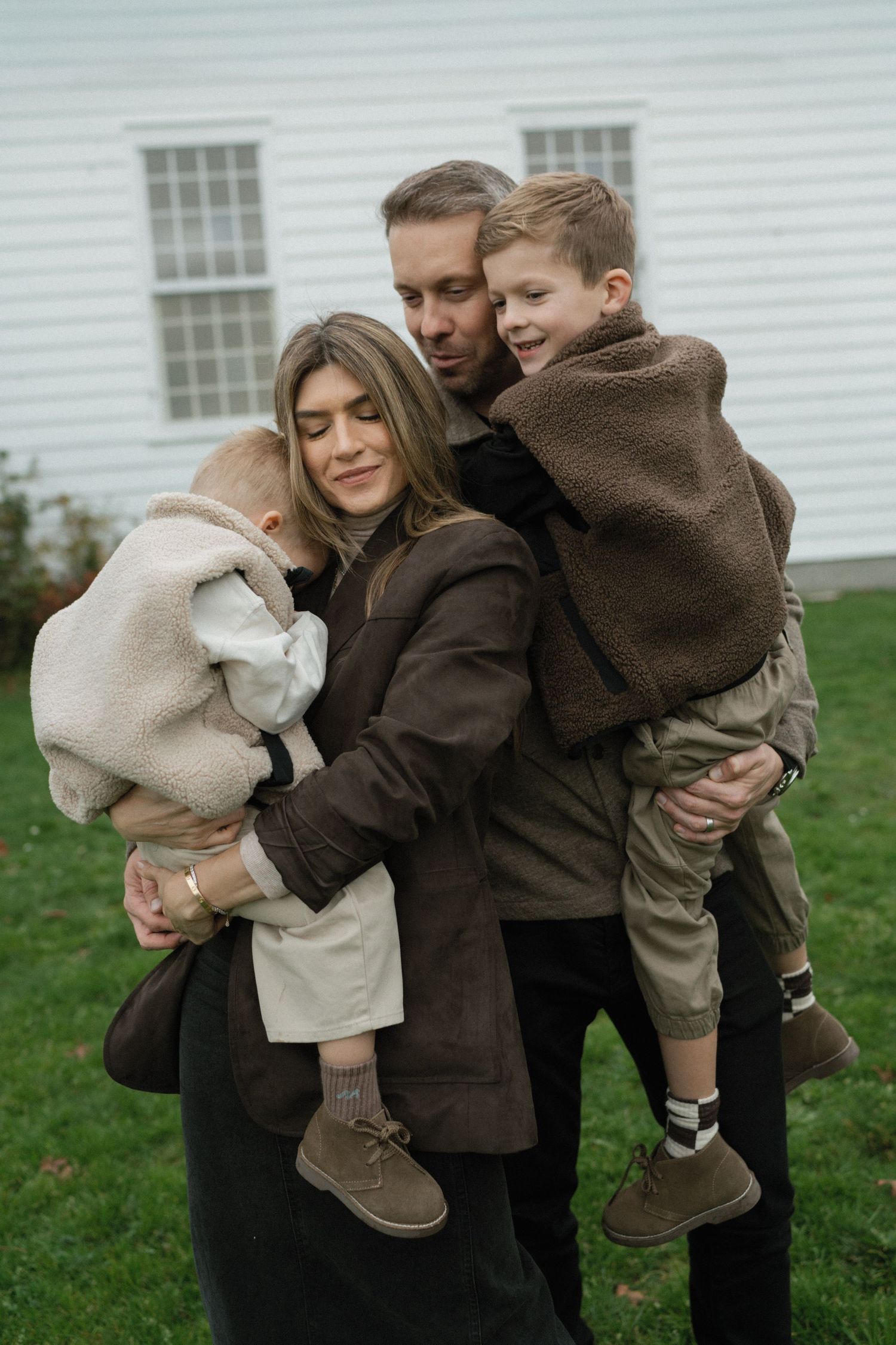 Family embracing together on grass in front of a white colonial-style building.
