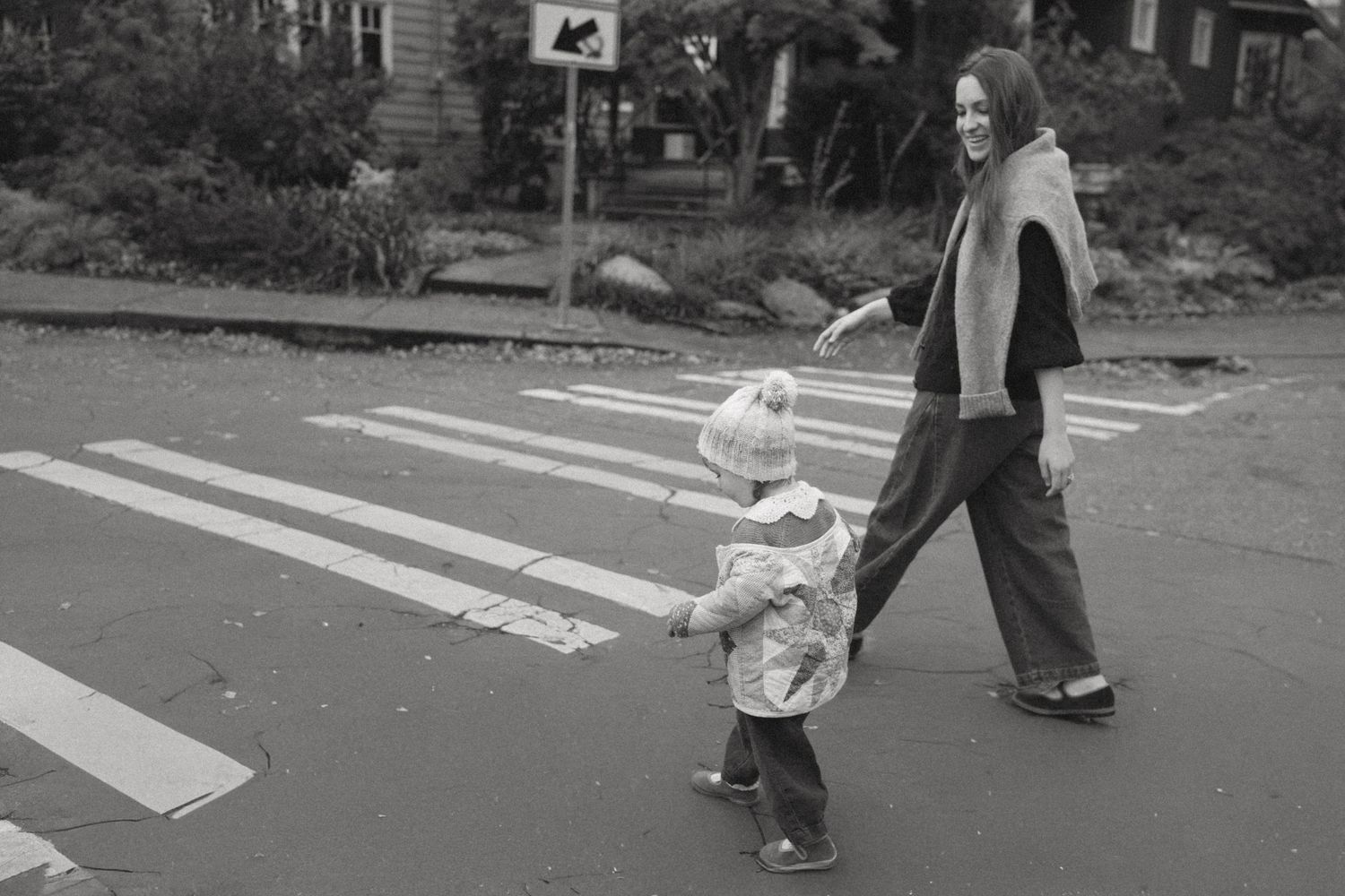 People walking across a crosswalk in casual attire on an urban street.