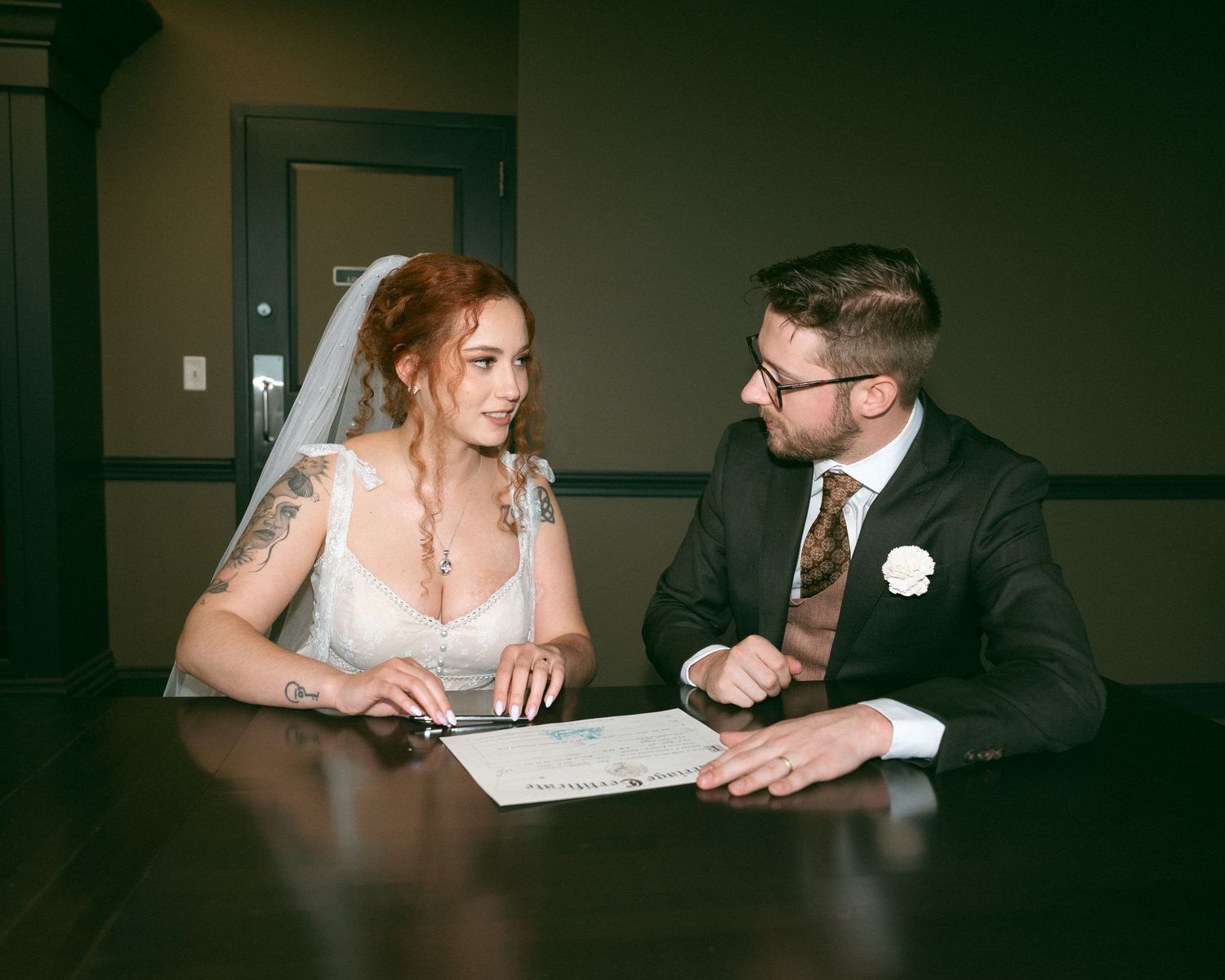 A couple shares quiet moments at a dark wooden table in dim lighting.