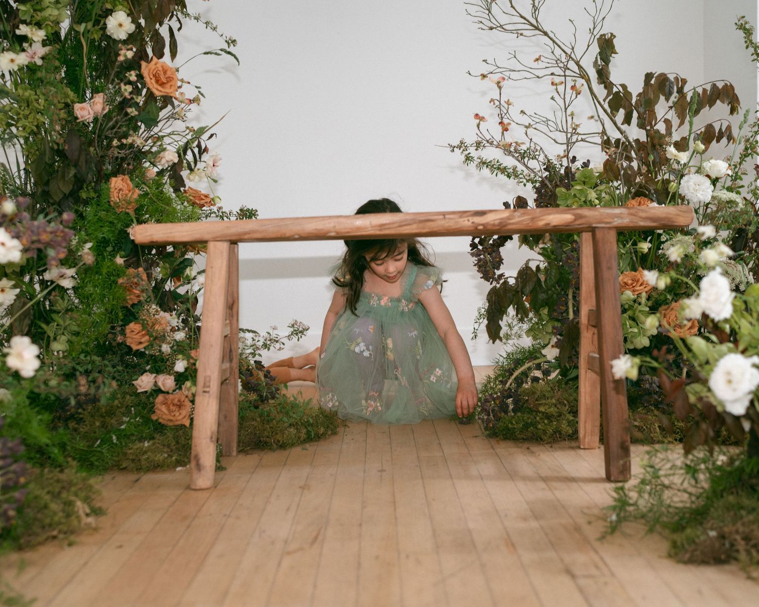 A floral arch with roses and greenery decorates a wooden platform.
