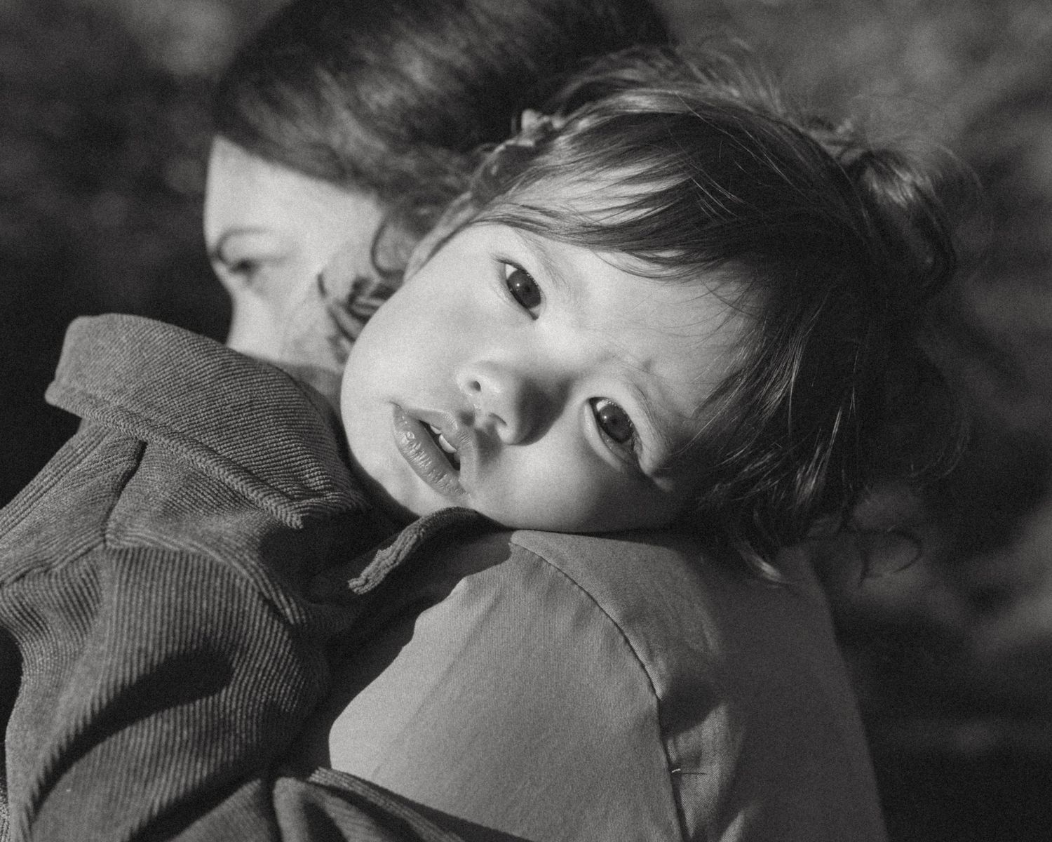 A young child in a dark jacket leans back with an expressive face in this black and white portrait.