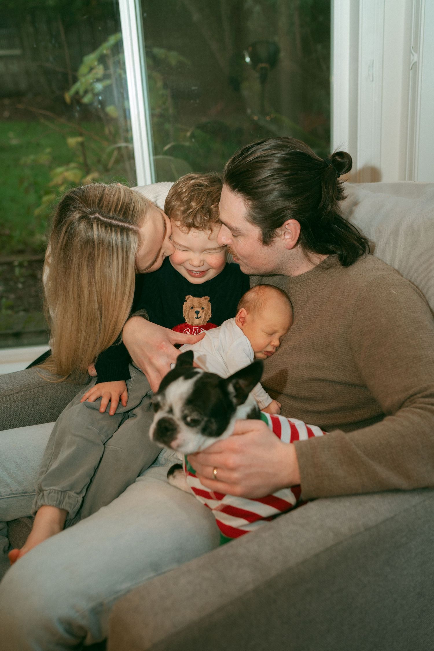 A couple sits together on a couch with a small dog wearing a striped shirt in a series of candid photos.