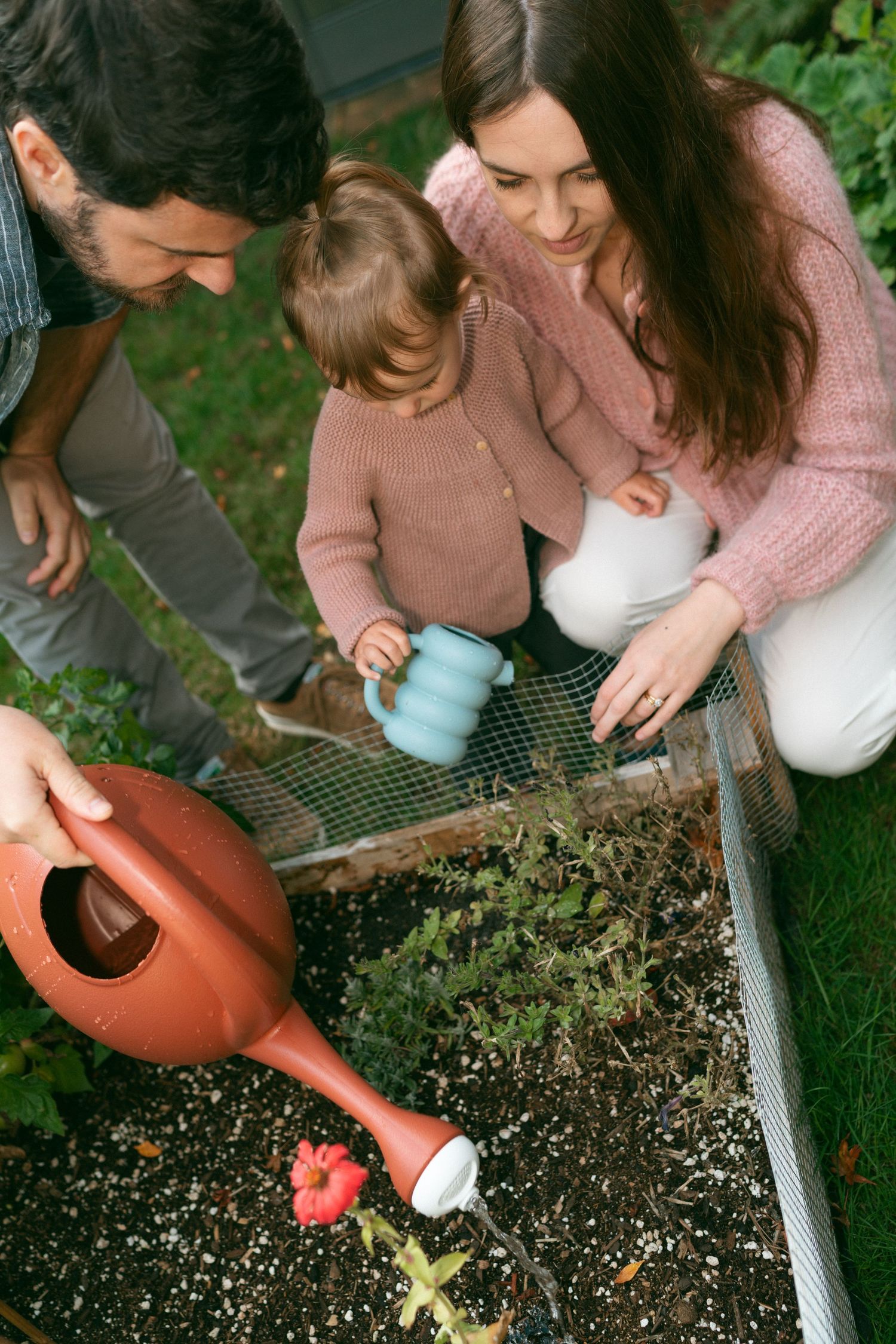 Person planting seeds in soil using a small watering can outdoors.
