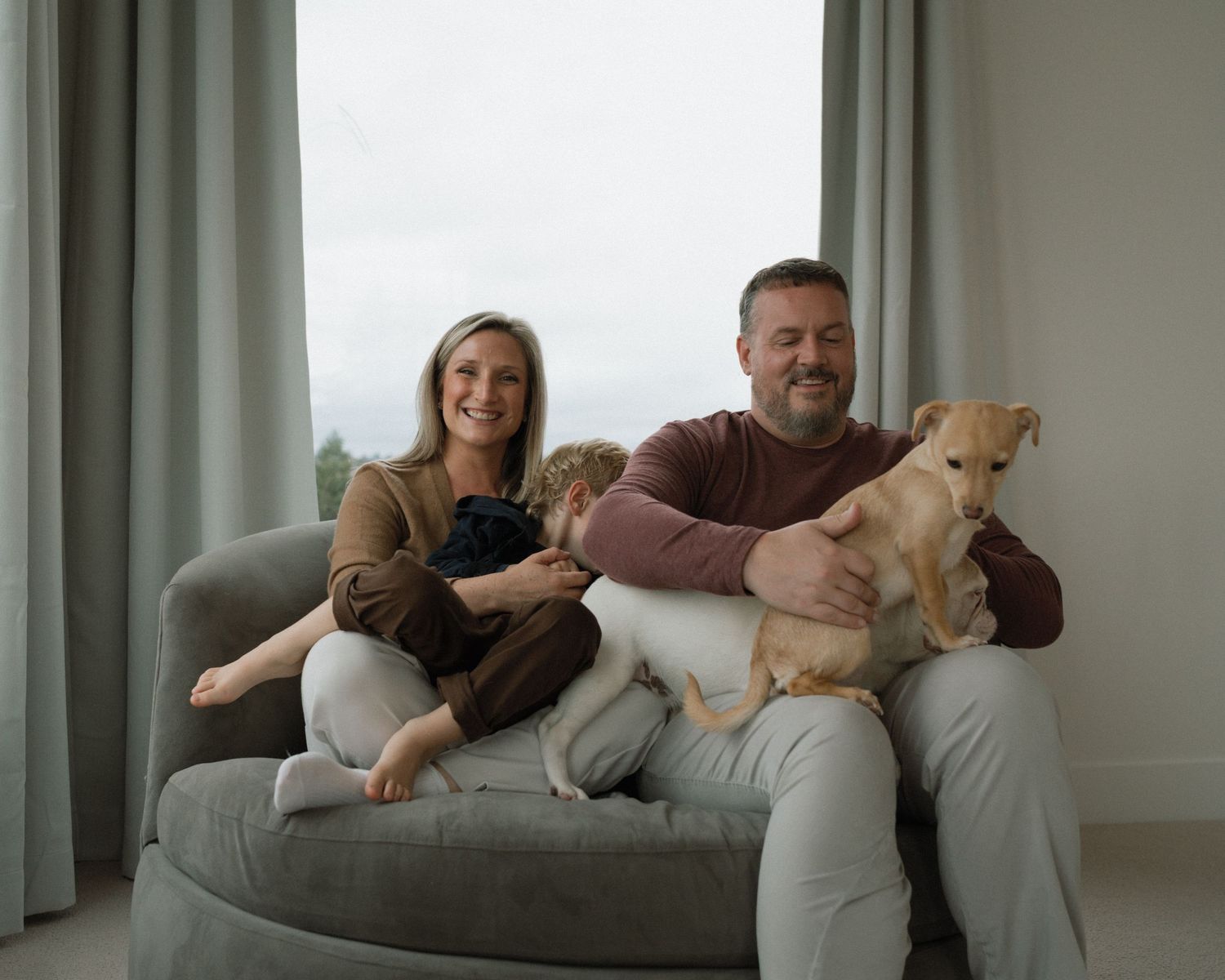 Family lounging together on a grey couch in a bright modern living room.