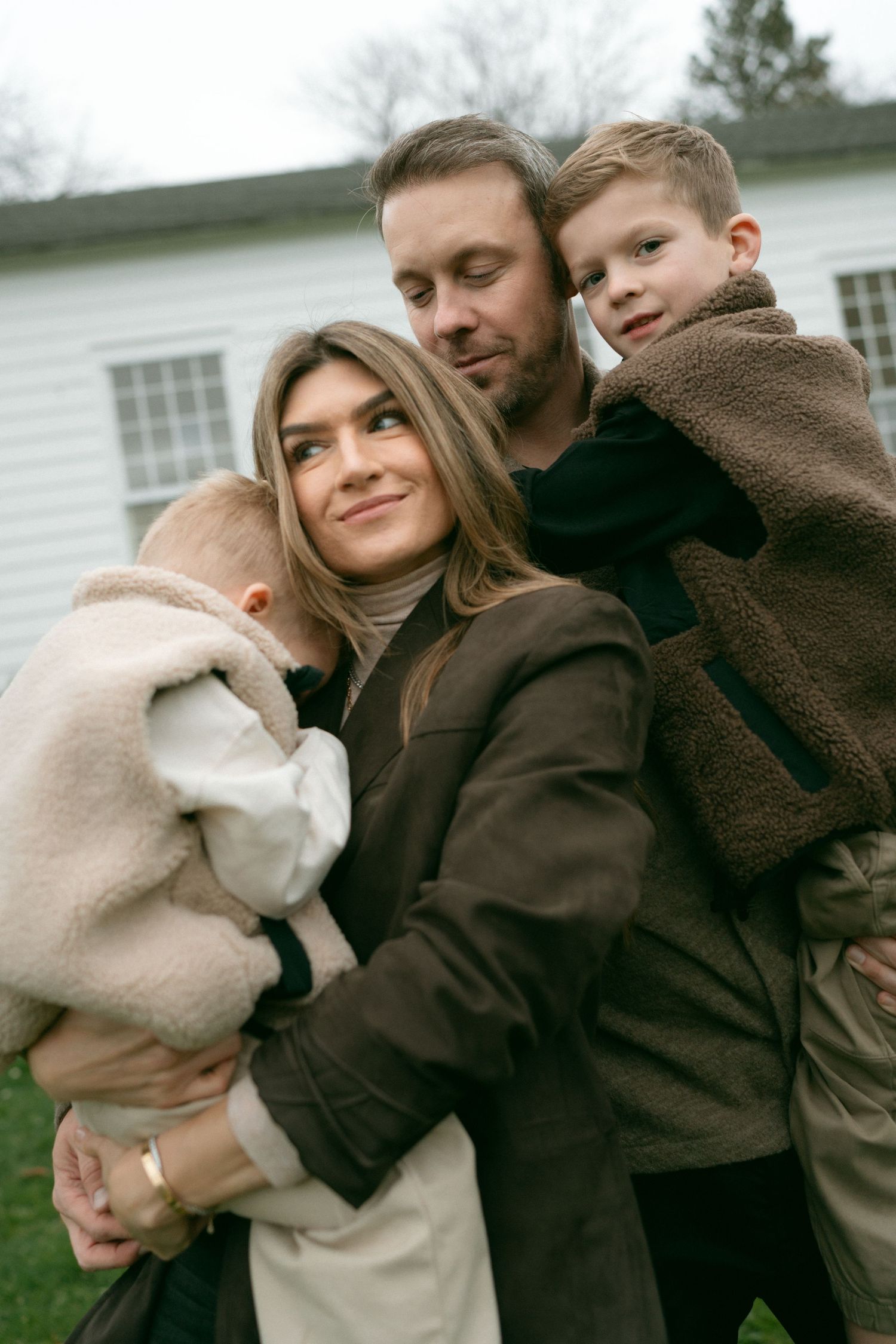 A group shares warm embraces while wearing cozy winter coats outdoors on a cloudy day.