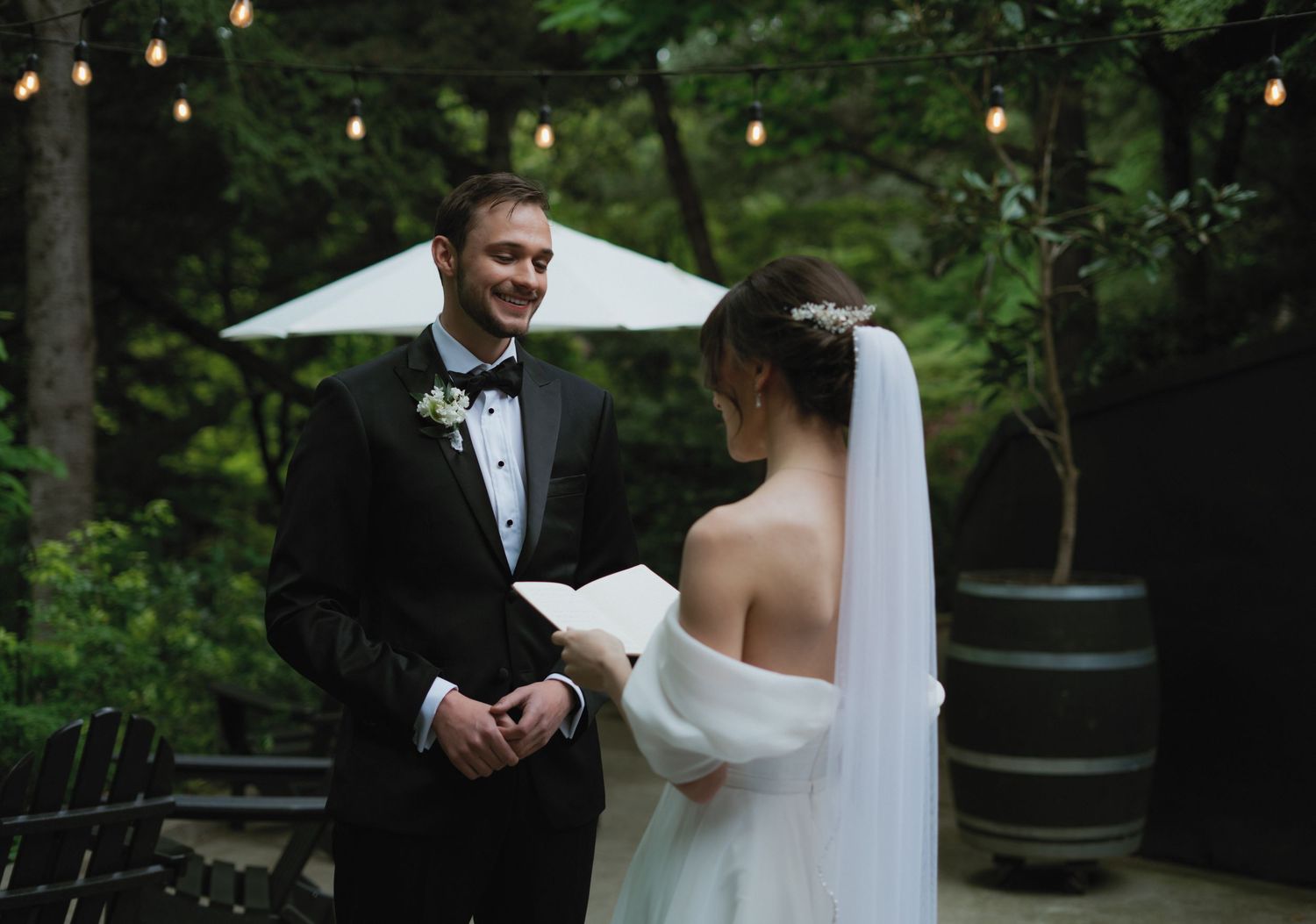 A romantic wedding couple shares intimate moments in a lush forest setting with string lights overhead.