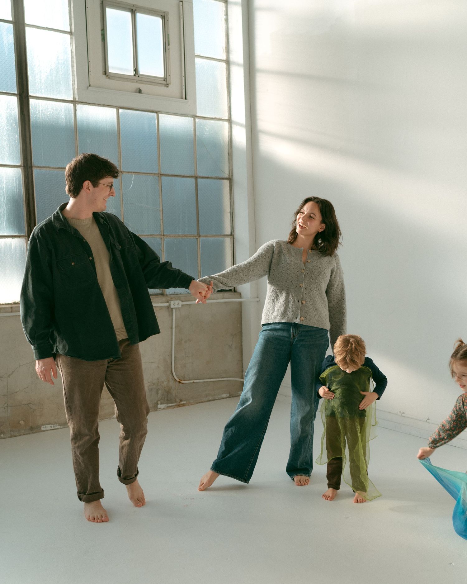 A group of dancers in casual attire perform modern dance movements in a bright white studio space.