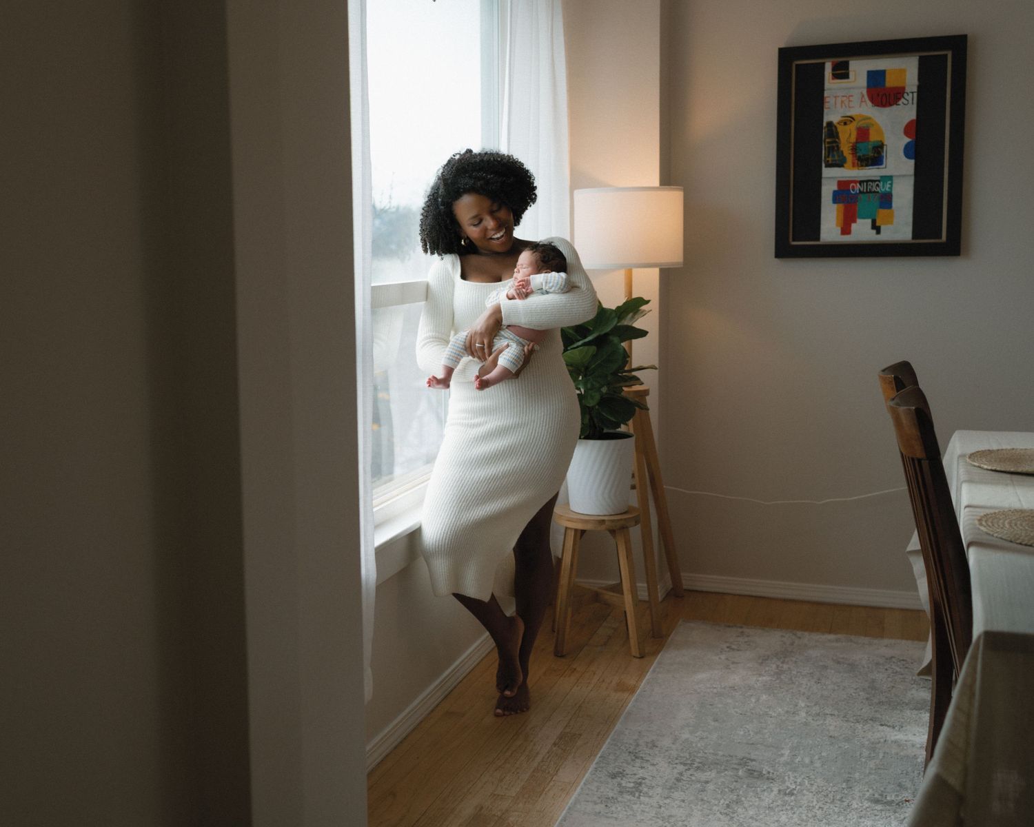 A woman in a white dress stands in a cozy living room with modern decor and natural lighting.